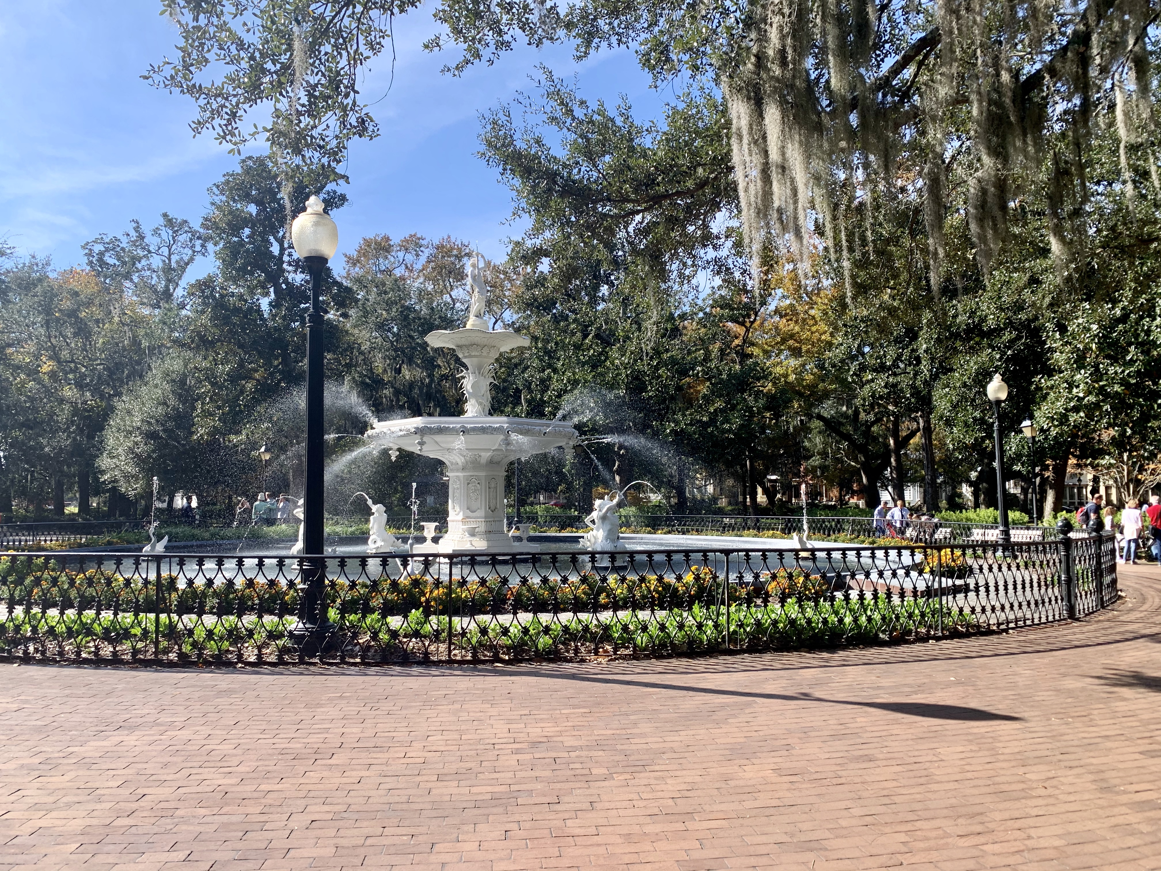 Circular white fountain in a park with trees hanging above on a sunny day
