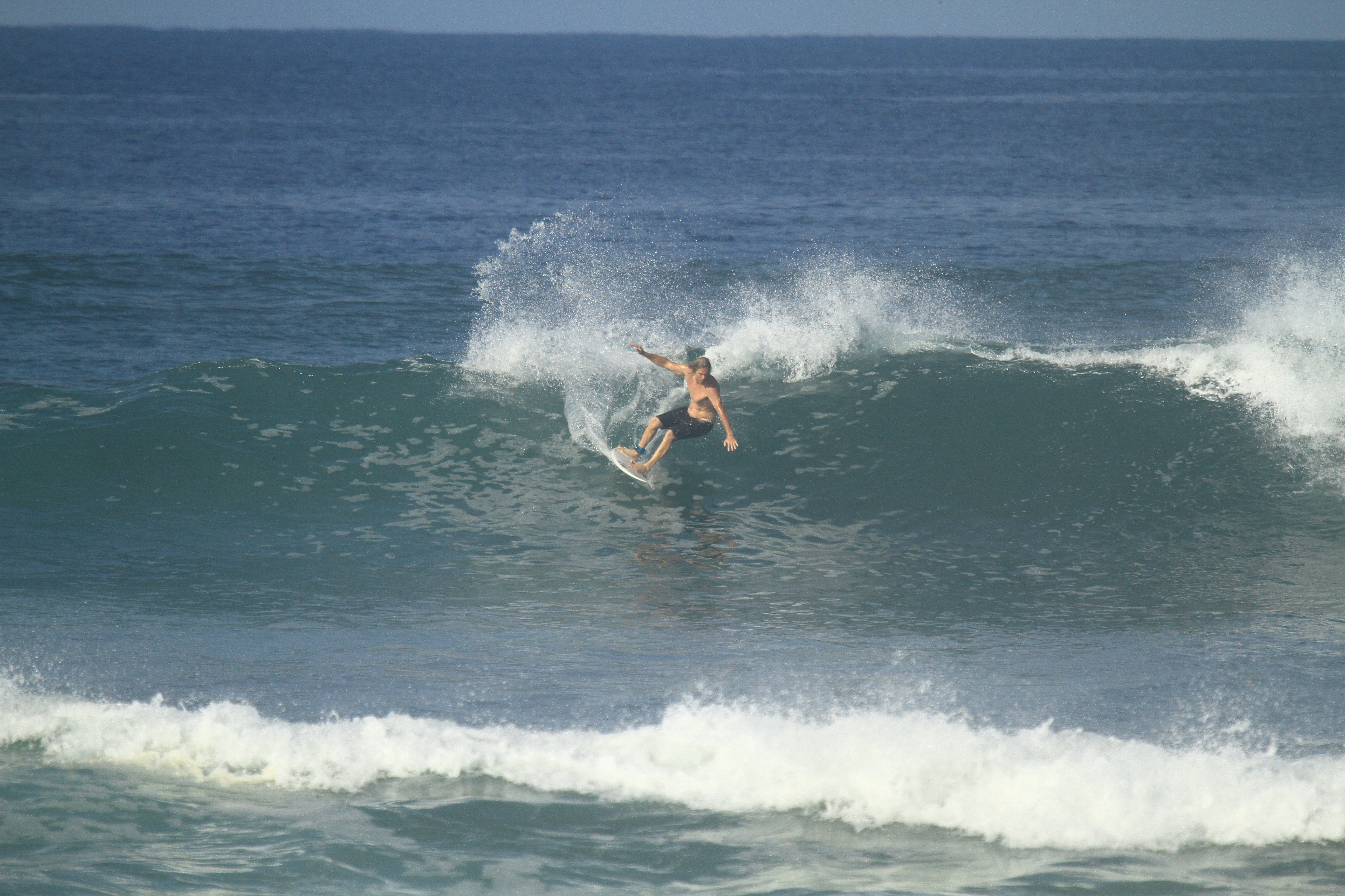 Advisor surfing a big wave in the ocean on a sunny day with a clear sky in the distance.