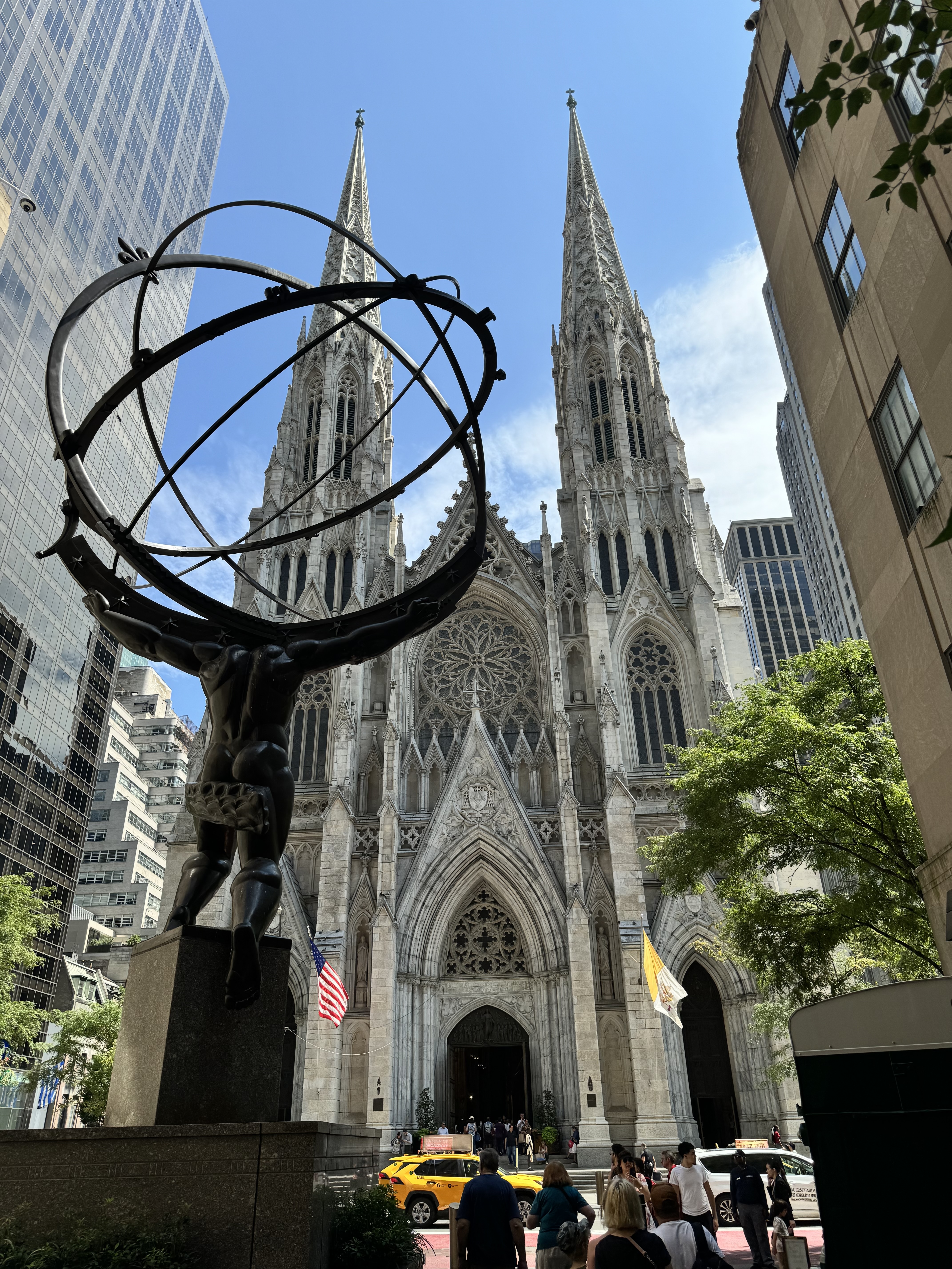 View of a beautiful cathedral in NYC with two spires and a metal sculpture in front under clear skies