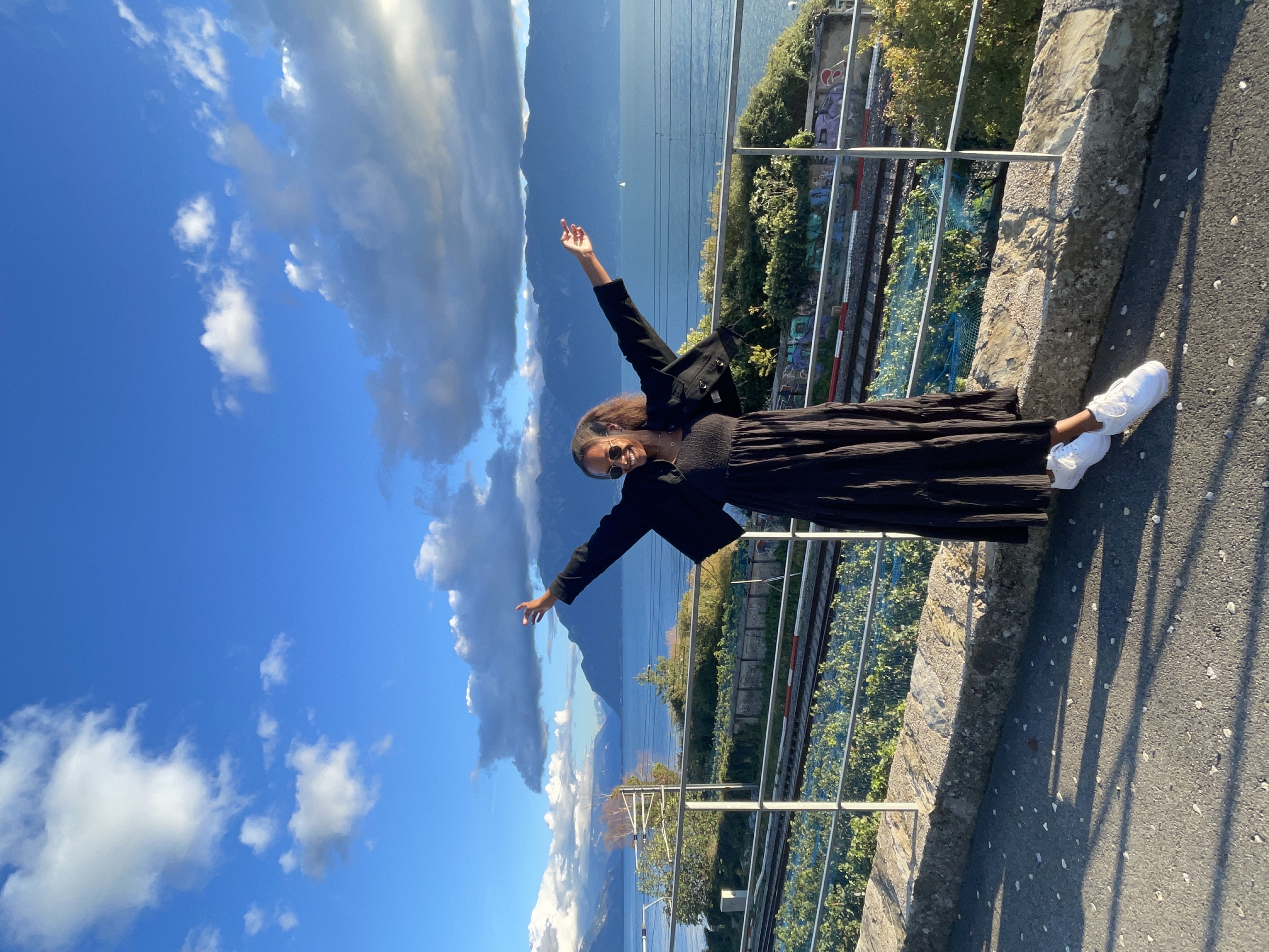 Advisor posing with arms raised at a viewpoint overlooking a sunny coastline and distant mountains