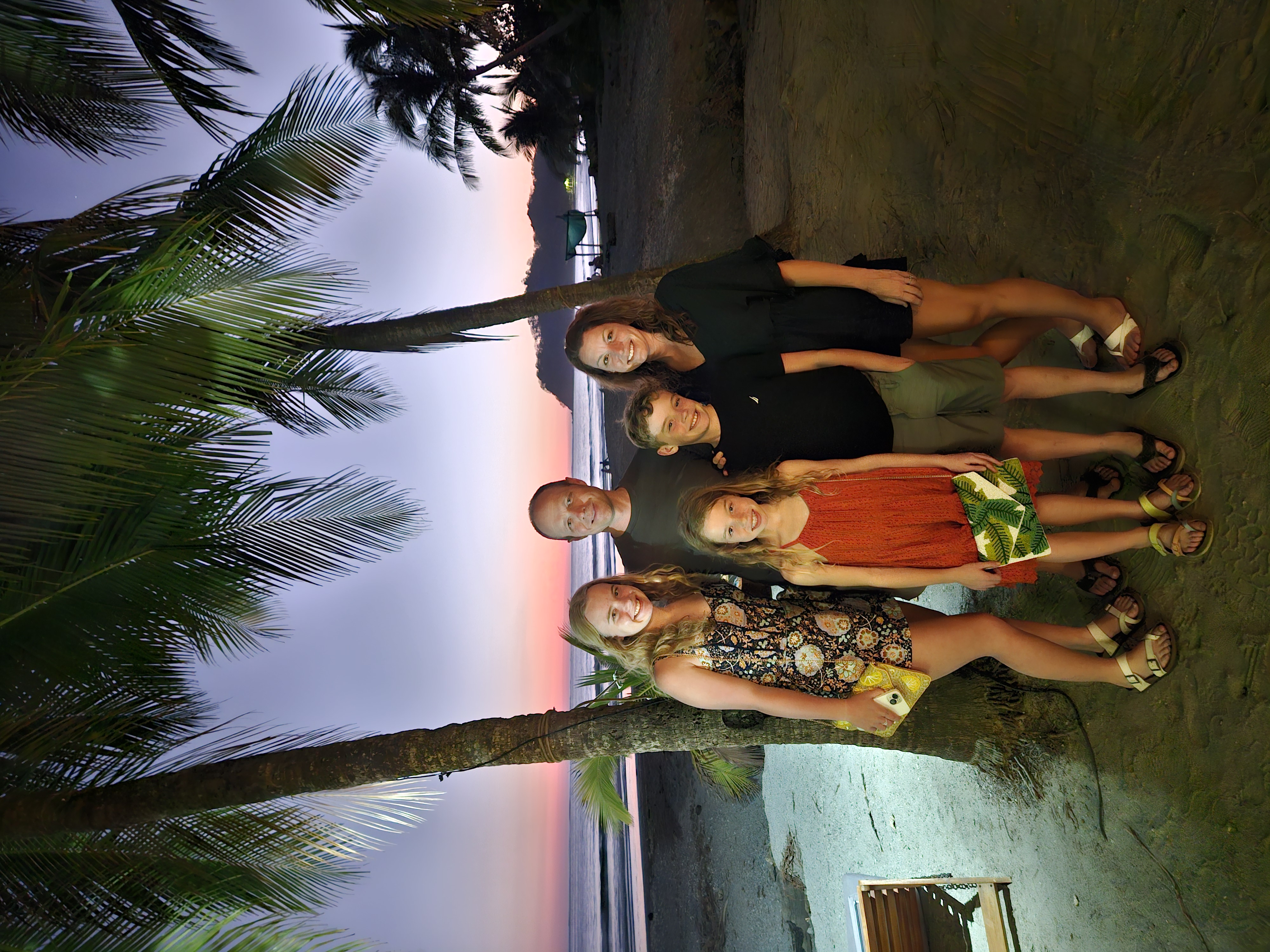Advisor and family posing together underneath a palm tree on the beach at sunset