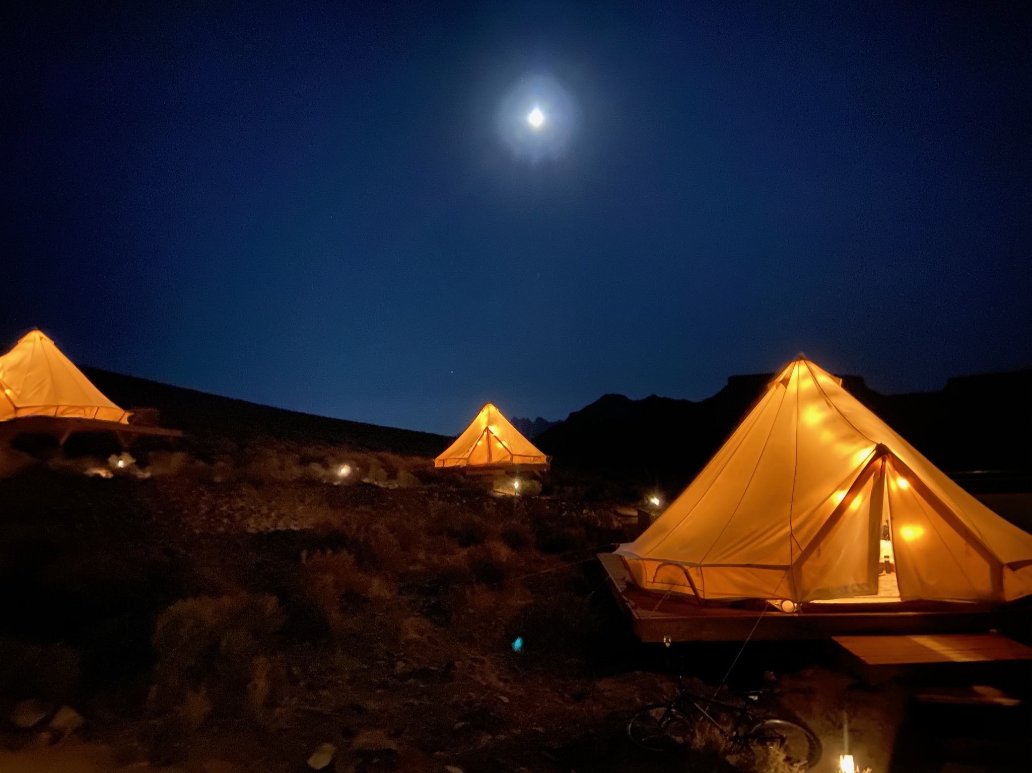 View of three glamping tents lit up at night under a full moon