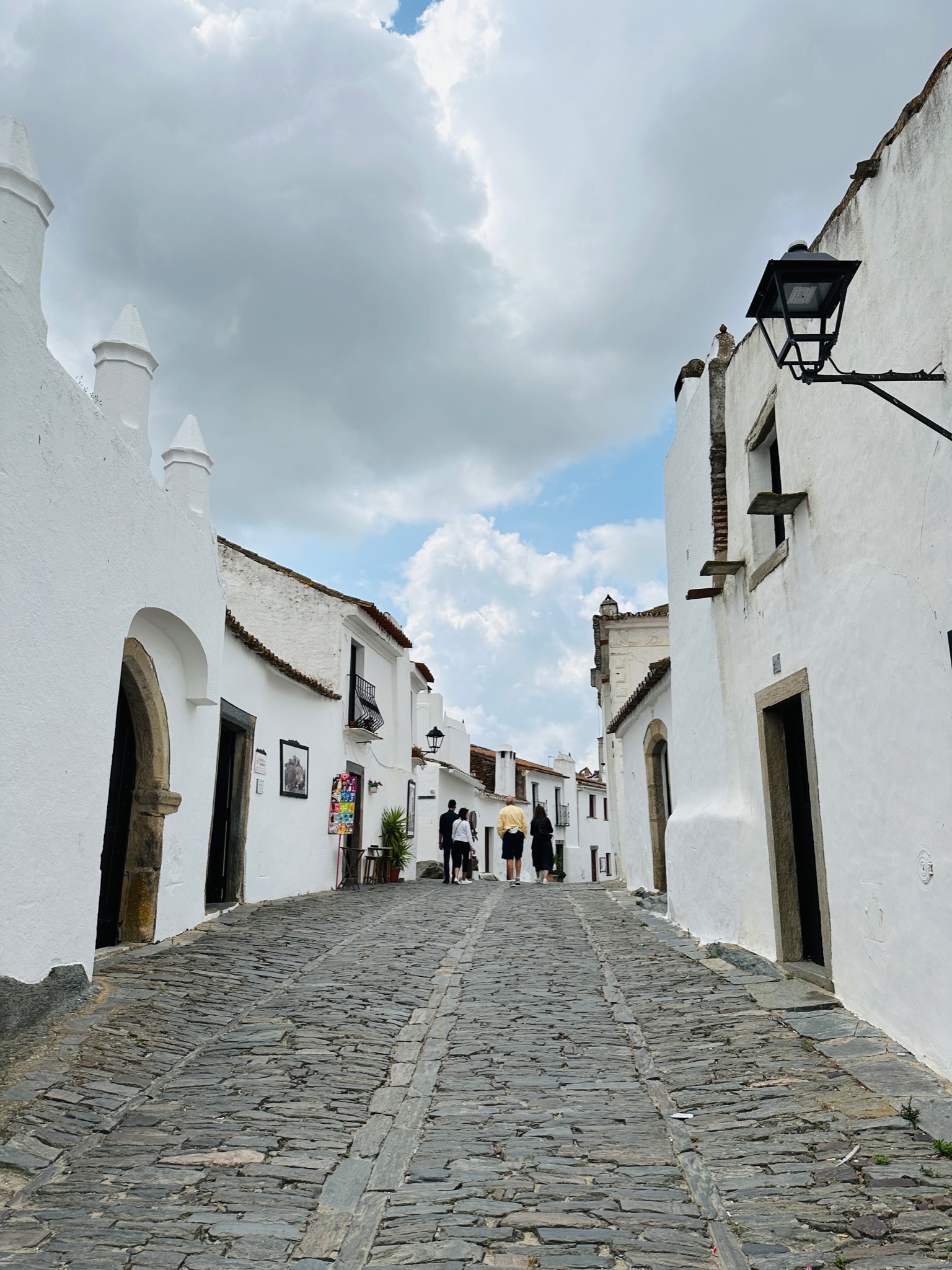 An empty cobblestone street between white buildings on a cloudy day