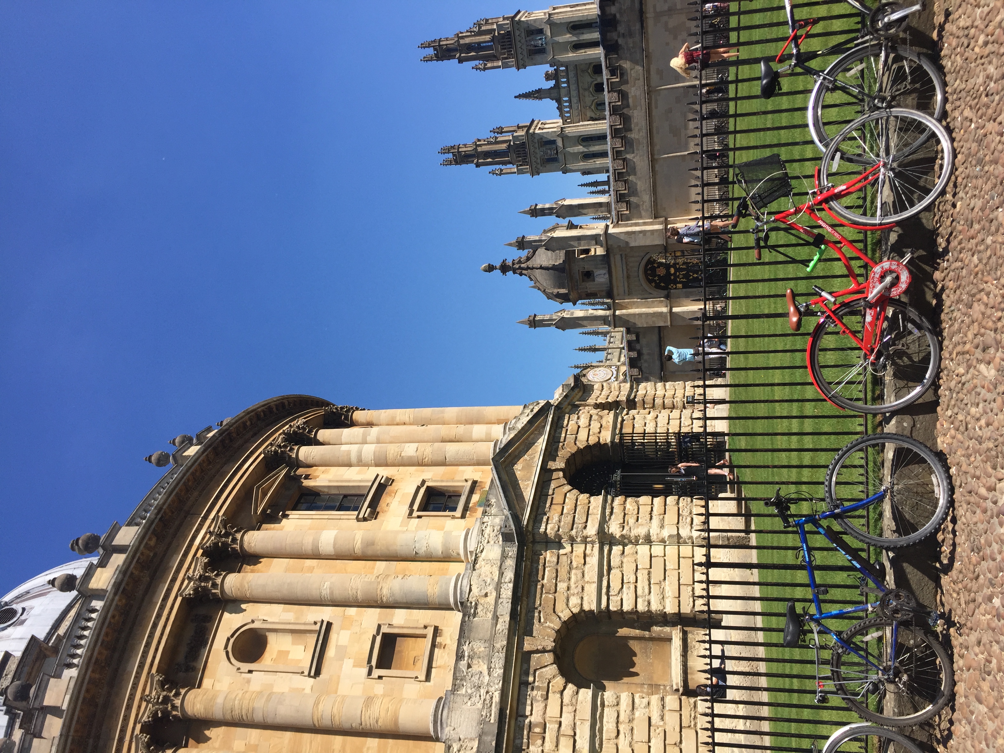 Bicycles parked against a gate with a large cathedral visible in the distance under clear skies