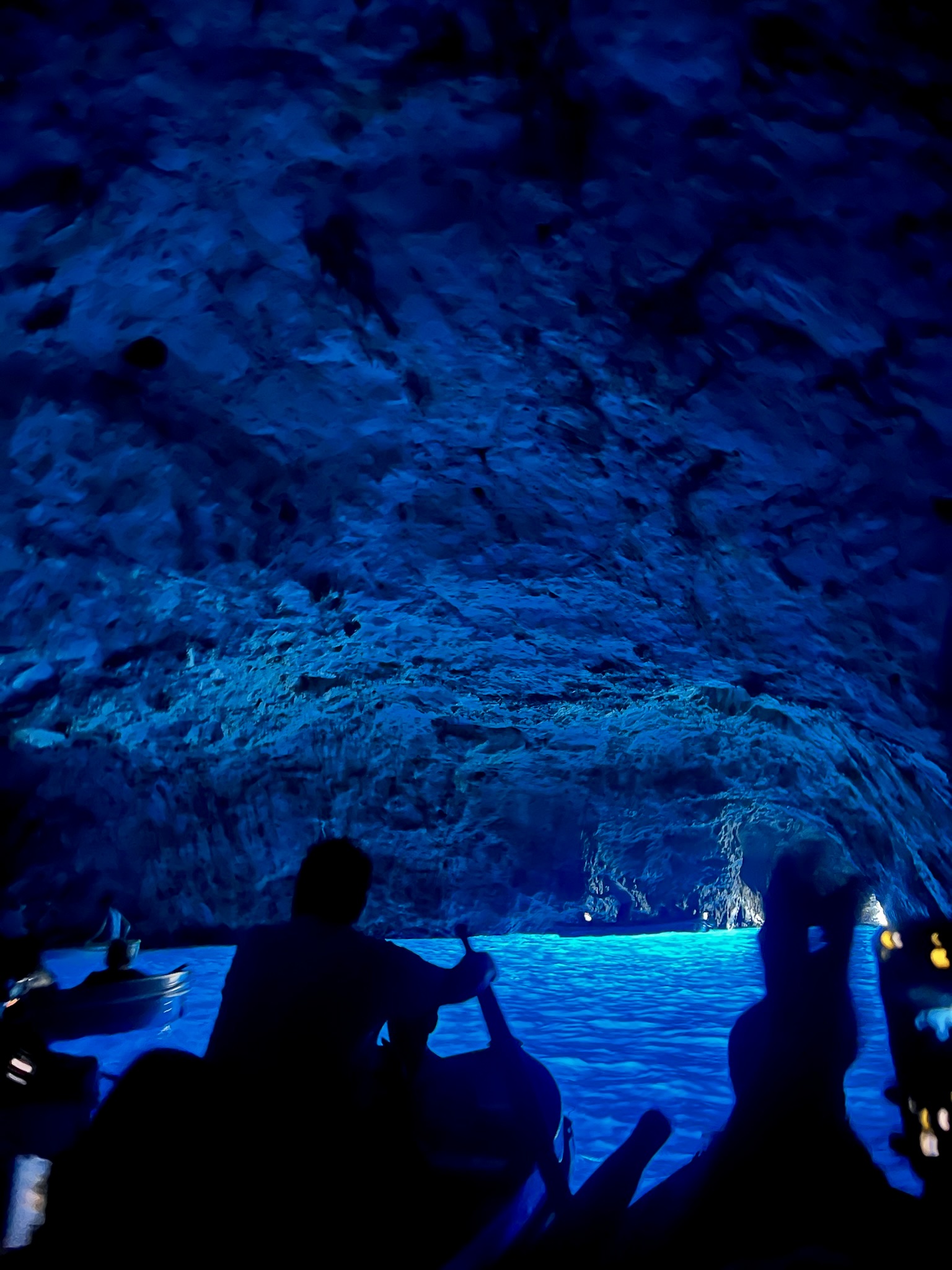 View of a boat sailing inside a dark cave with bright blue water