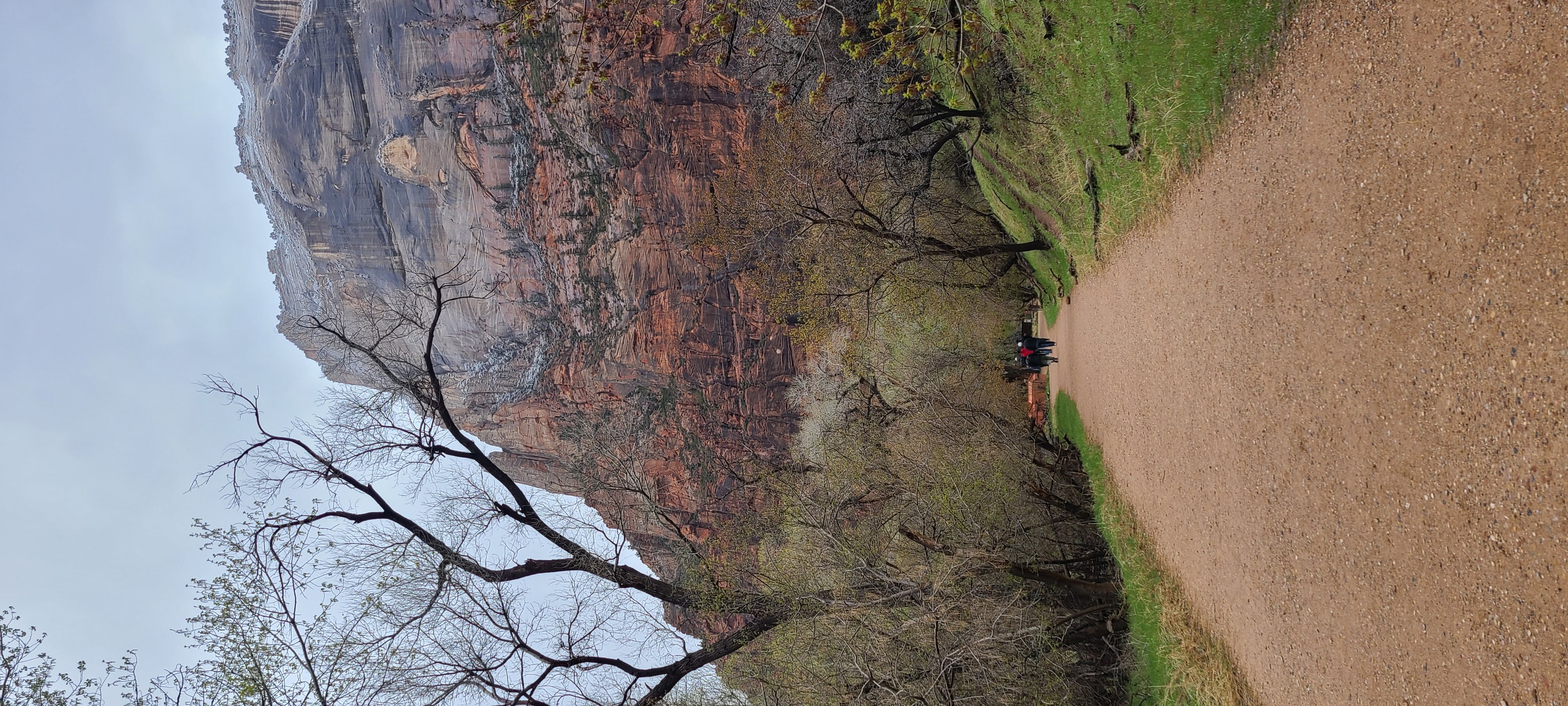 View of an empty dirt trail leading towards a rocky mountain on a cloudy day