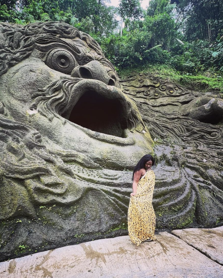 Advisor in a yellow dress standing before a large face with open mouth carved into a rock