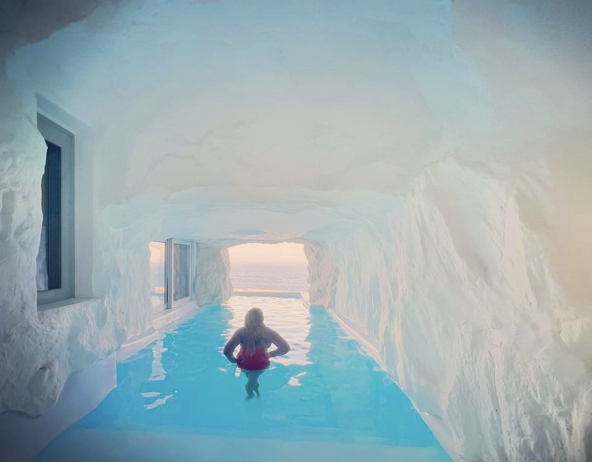 Advisor standing in waist-deep bright blue water in a cave with sunlight streaming through the entrance