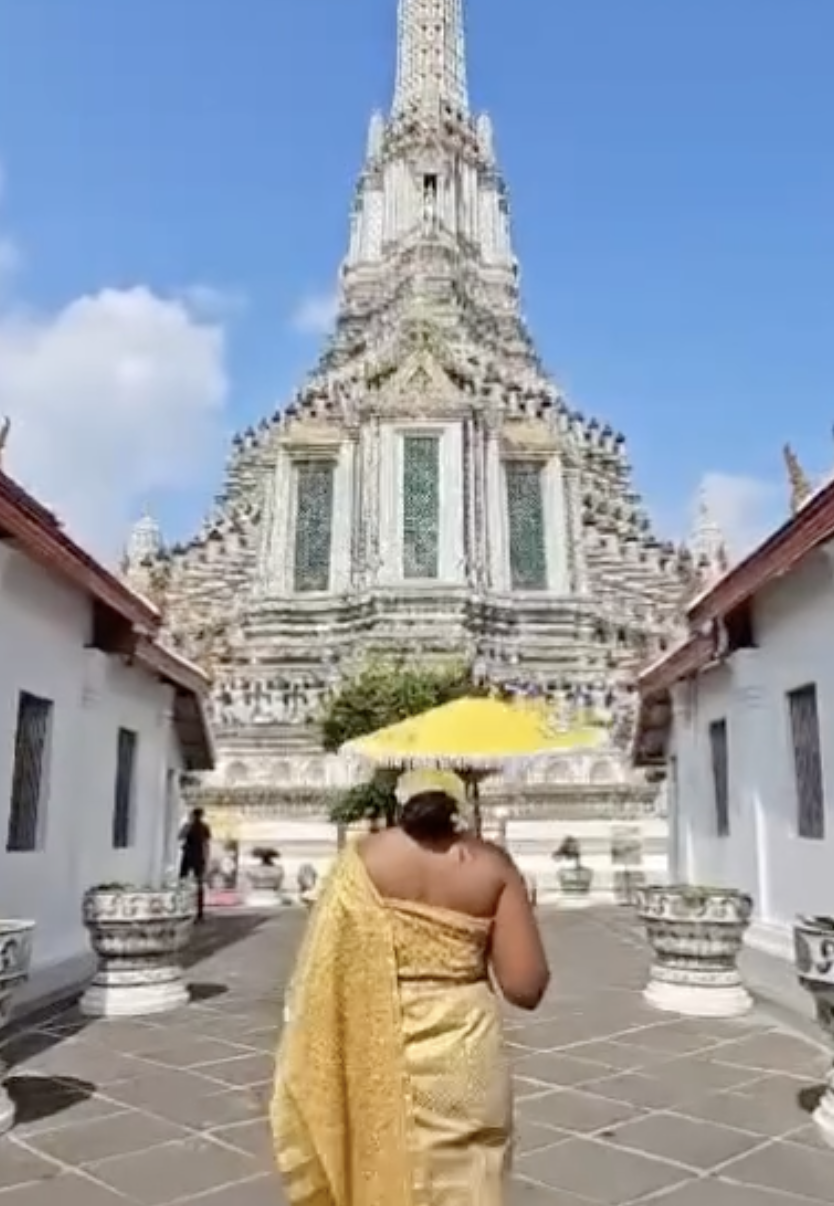 Advisor walking towards a large white temple with a yellow umbrella in hand on a sunny day