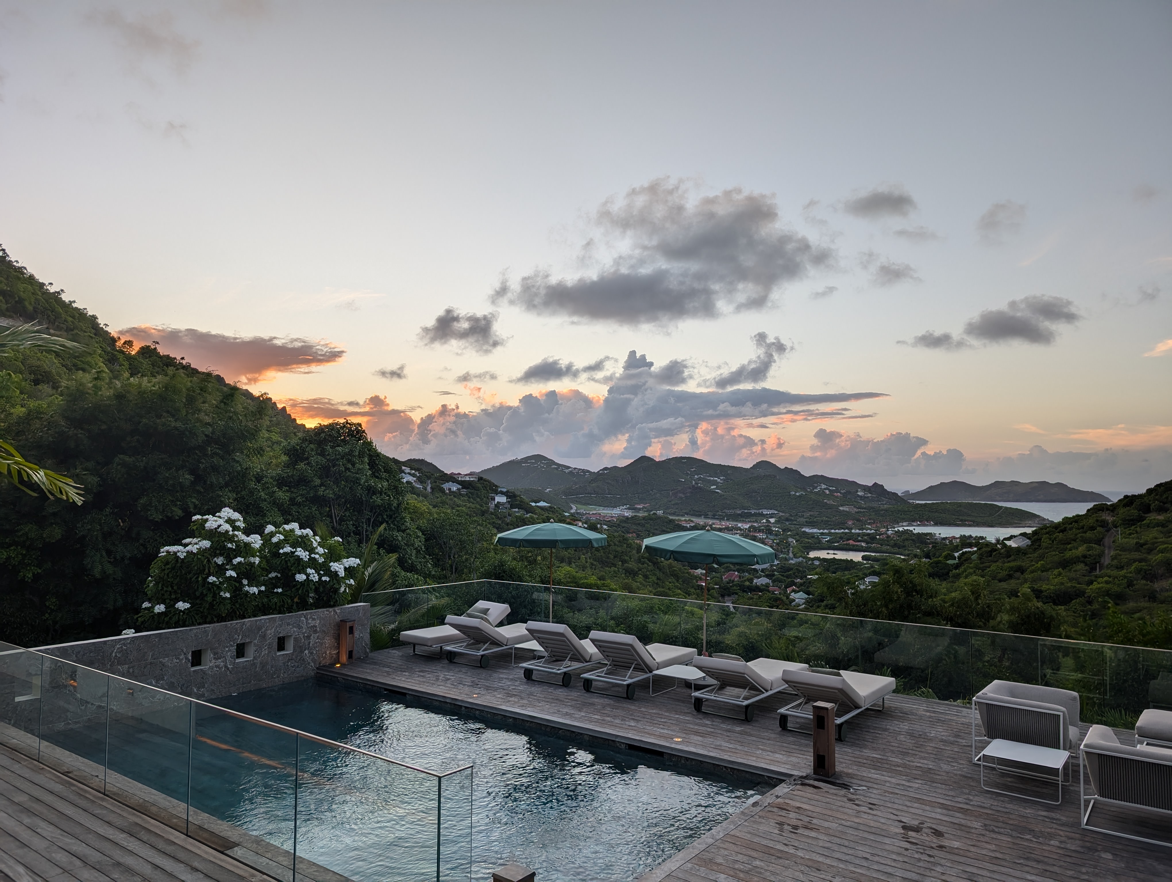 A view of a hotel pool at dusk with foliage and a mountain scape in the distance.