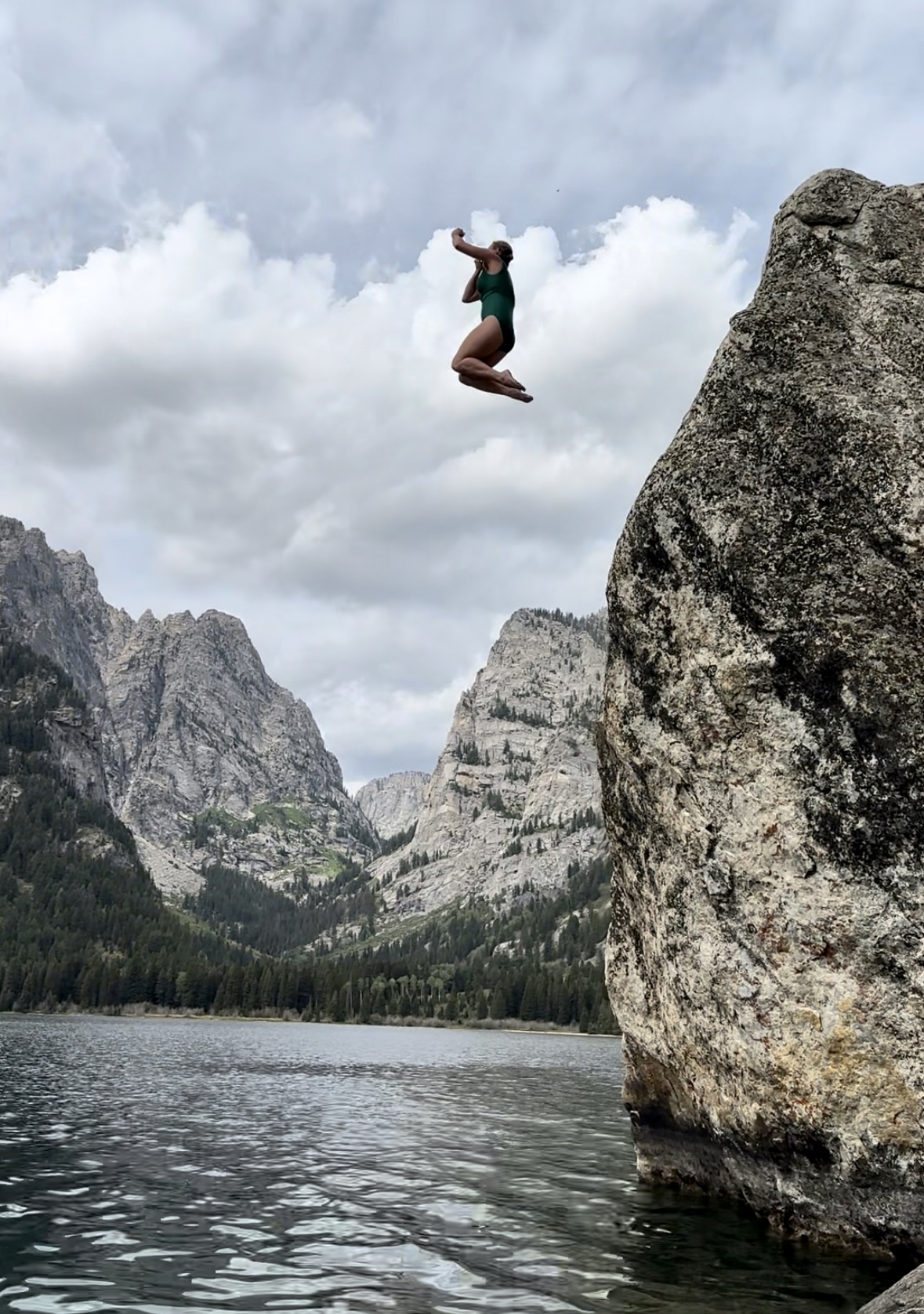 Advisor mid-air after jumping off a big rock on a cloudy day
