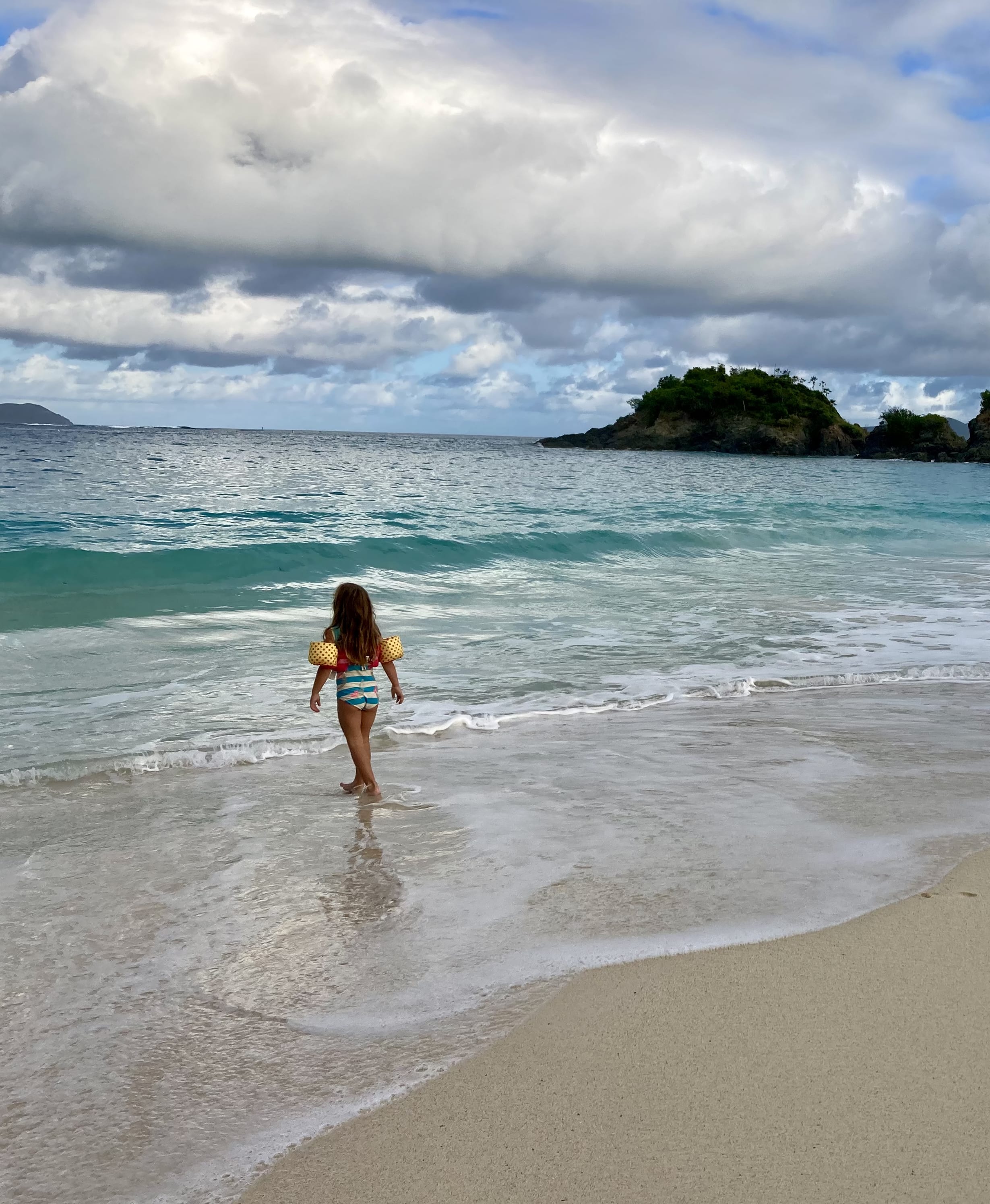 Advisor’s daughter walking into a calm turquoise sea from an empty beach