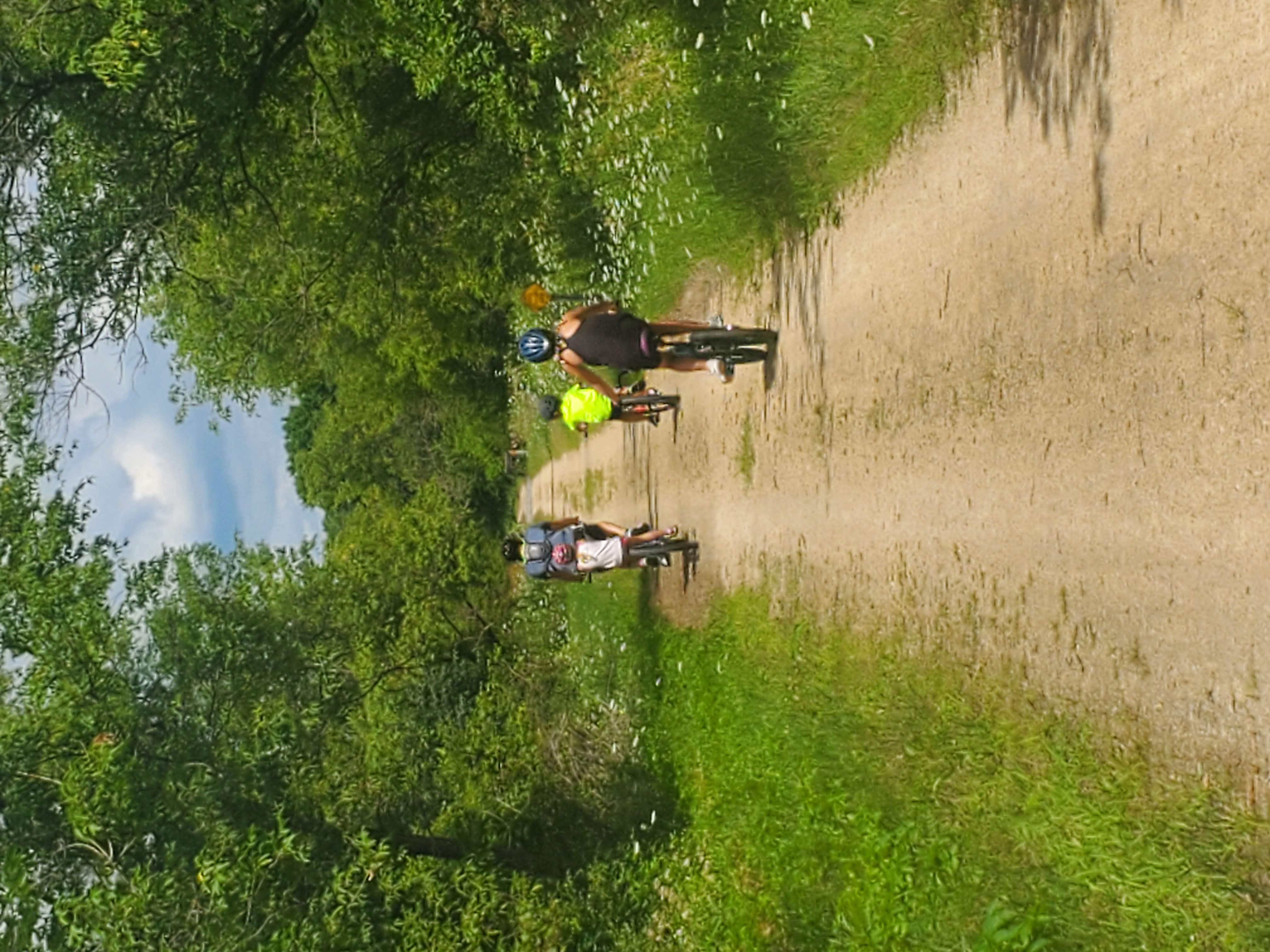 Advisor’s family riding bikes along a dirt path lined with leafy trees