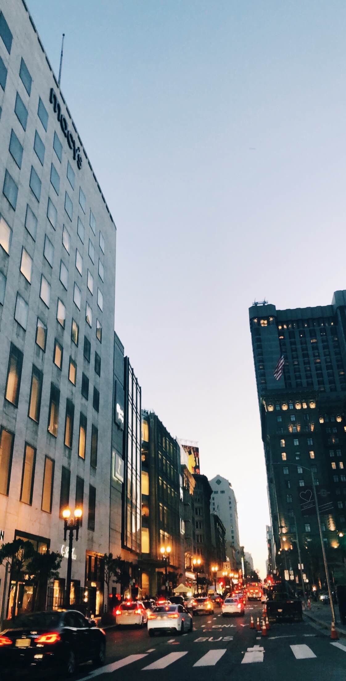 View of a city street at dusk lined with large buildings and traffic