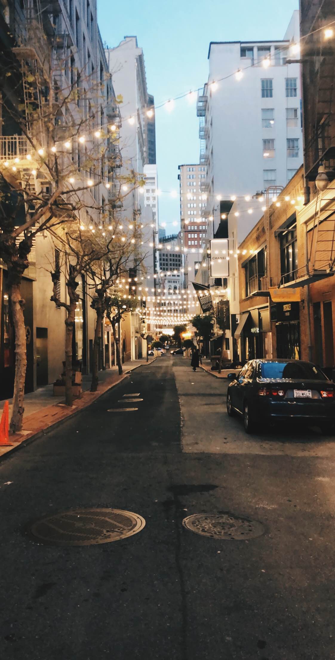 View of a city street with outdoor seating and string lights hanging above