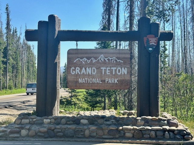View of a wooden sign for Grand Teton National Park under sunny skies