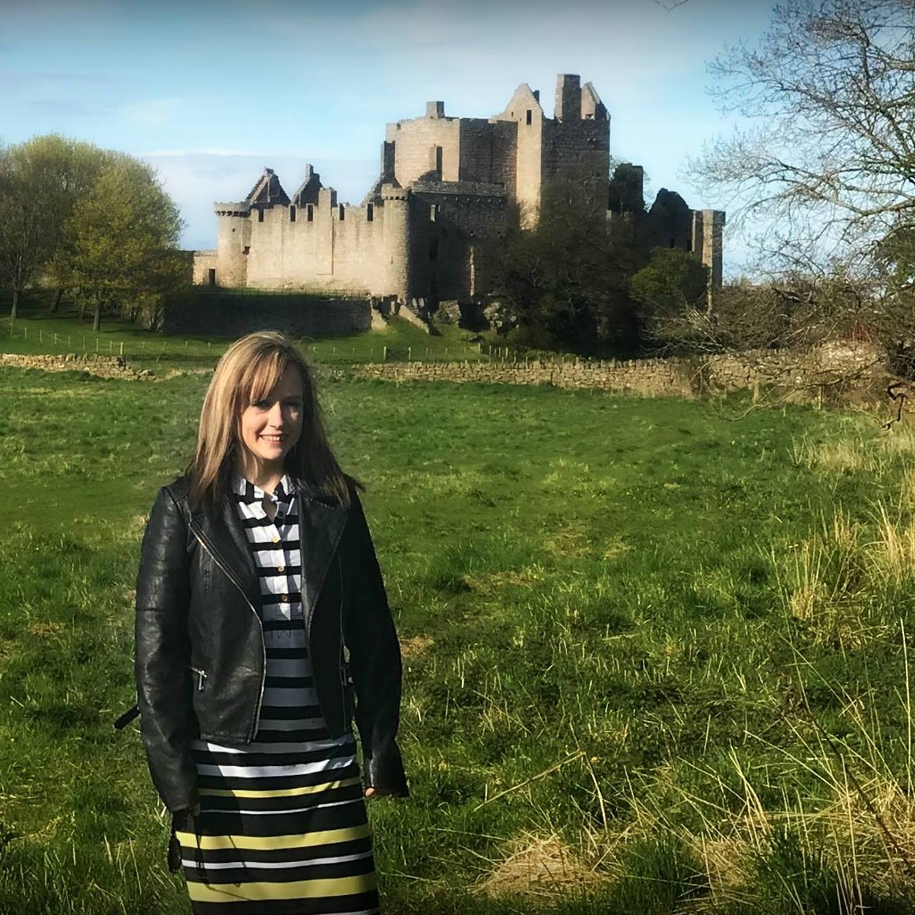 Advisor in a black and white striped dress standing in a grassy field with a large castle in the distance