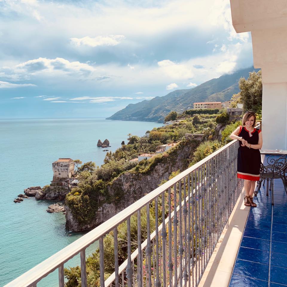 Advisor leaning on a balcony railing overlooking a stunning coastline with cliffs and a calm sea