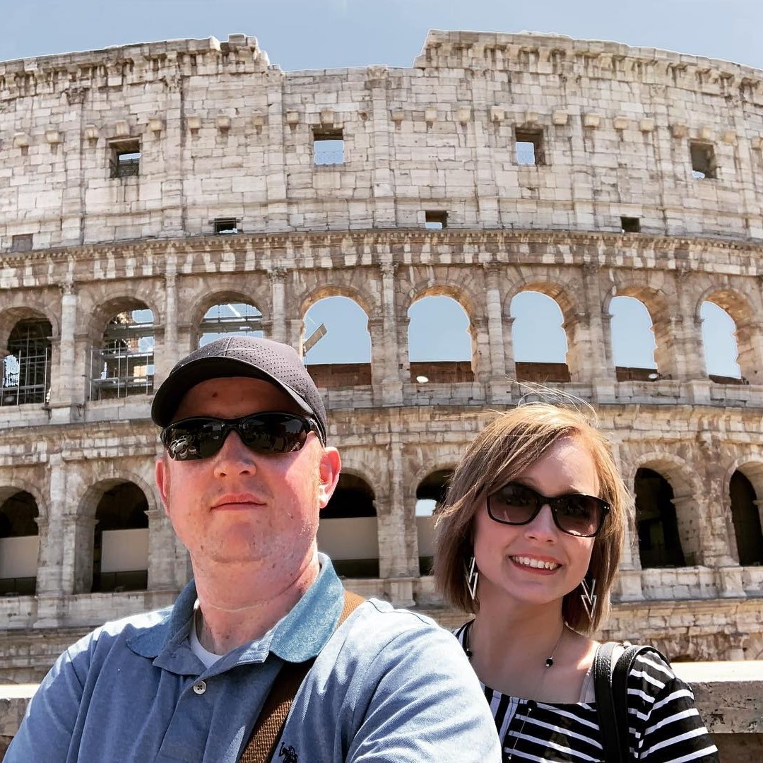 Advisor and partner smiling together in front of the Colosseum on a sunny day in Rome