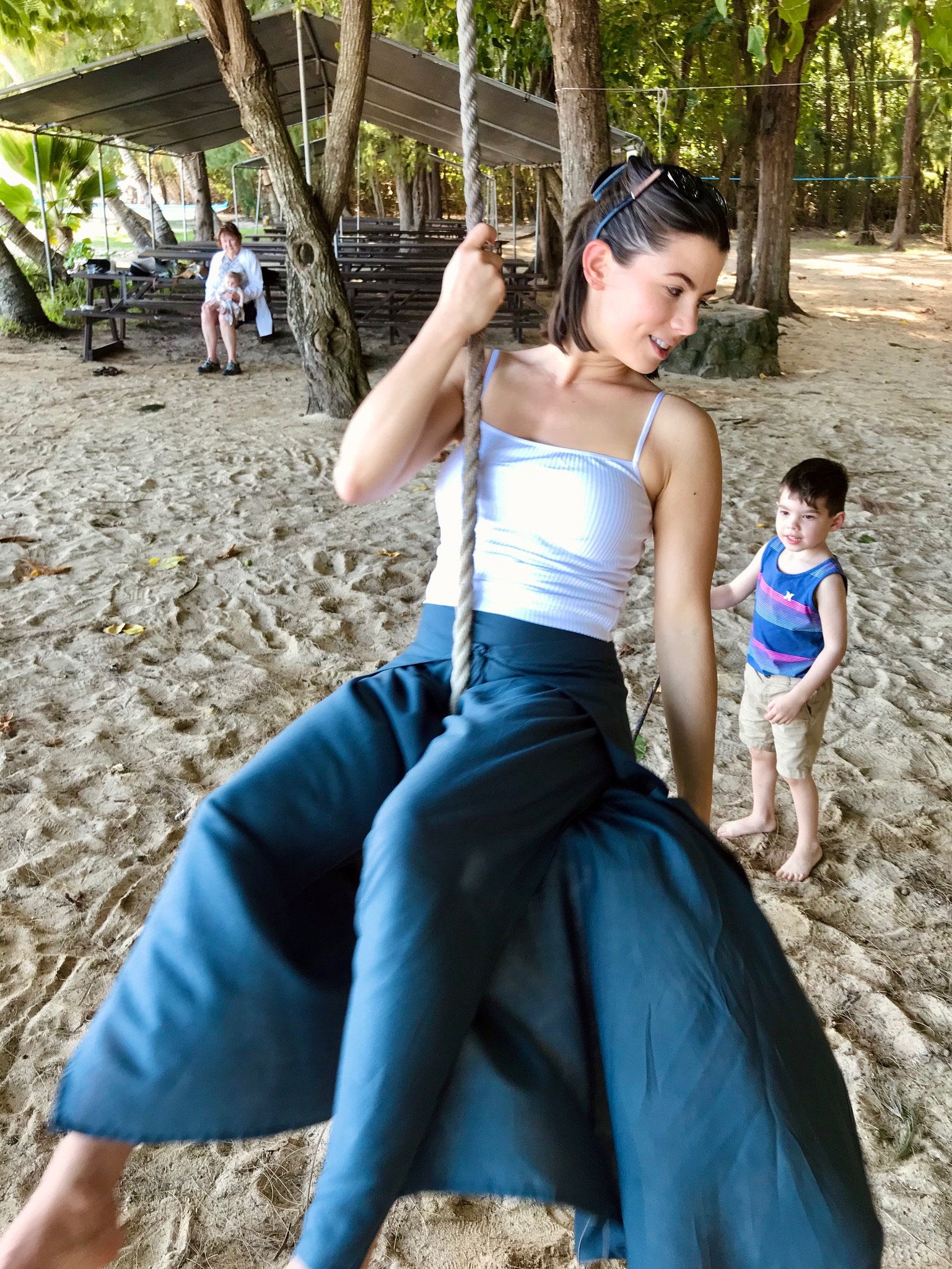 Advisor sitting on a rope swing on a sandy beach with a little boy standing beside her
