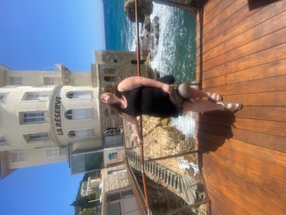 Debbie posing on a ledge outdoors by the ocean.
