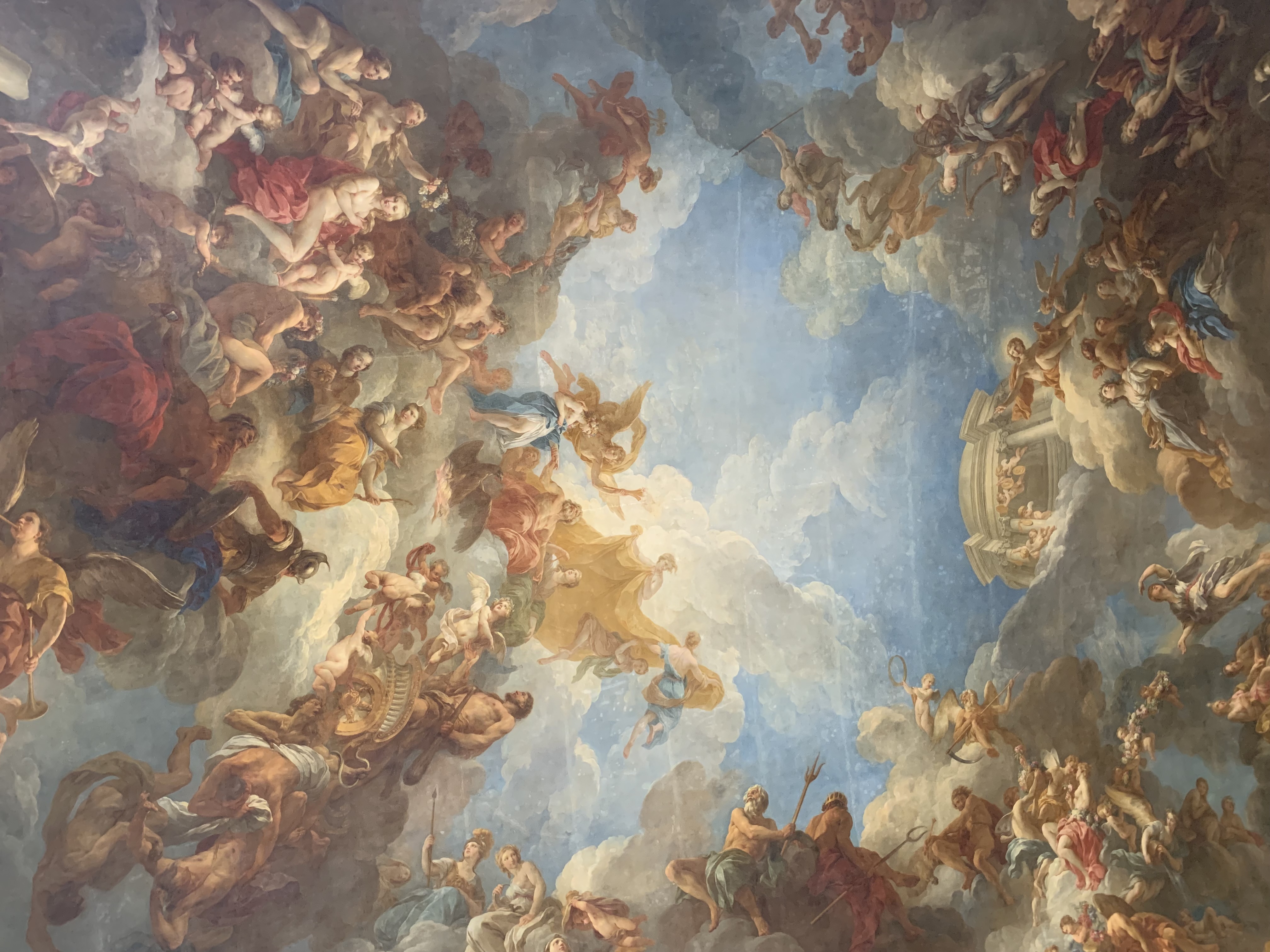 View of a beautifully ornate painted ceiling depicting a light blue cloudy sky with cherub-like figures