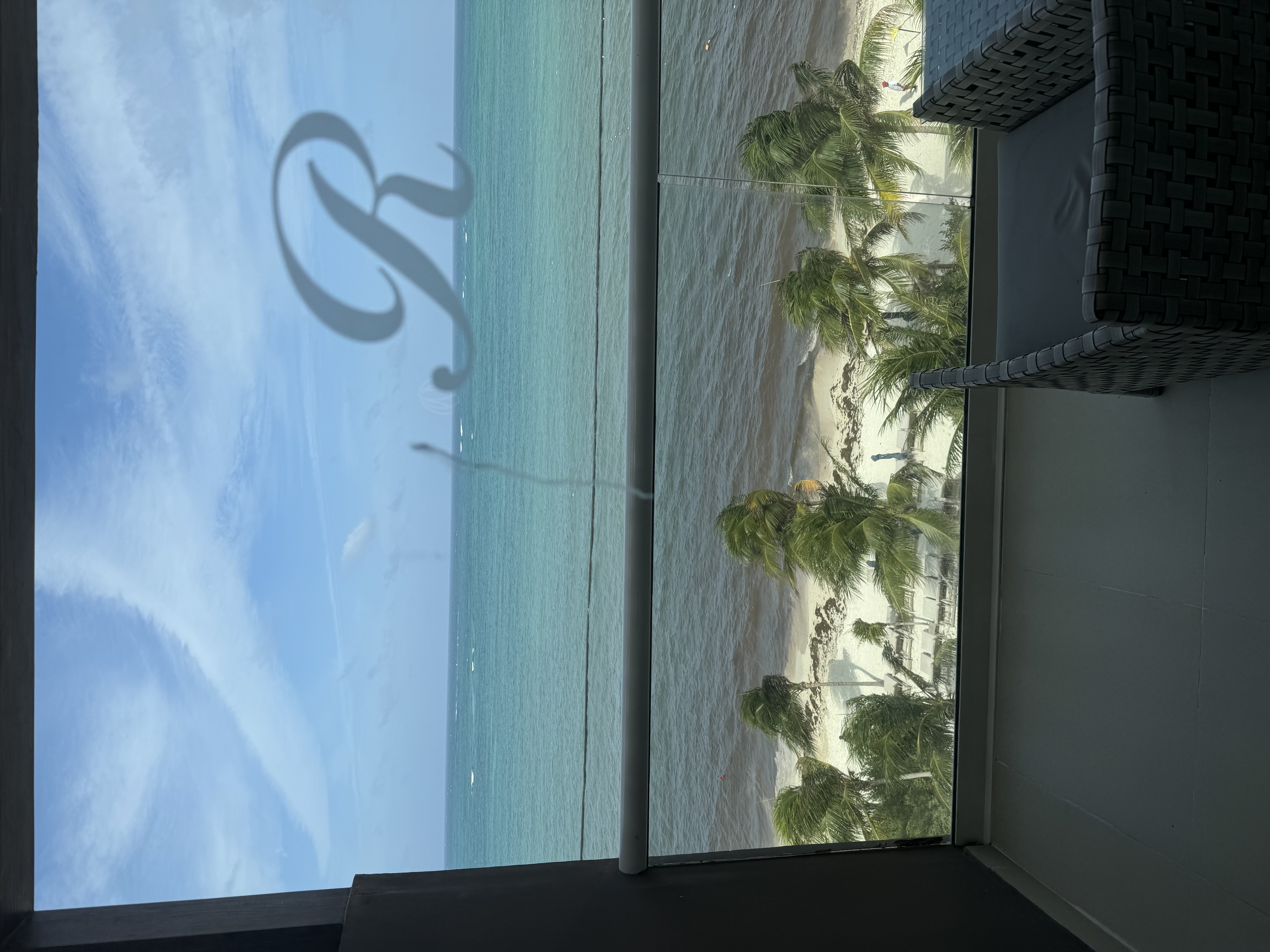 A view overlooking a white sand beach with palm trees and a calm ocean on a partly cloudy day.
