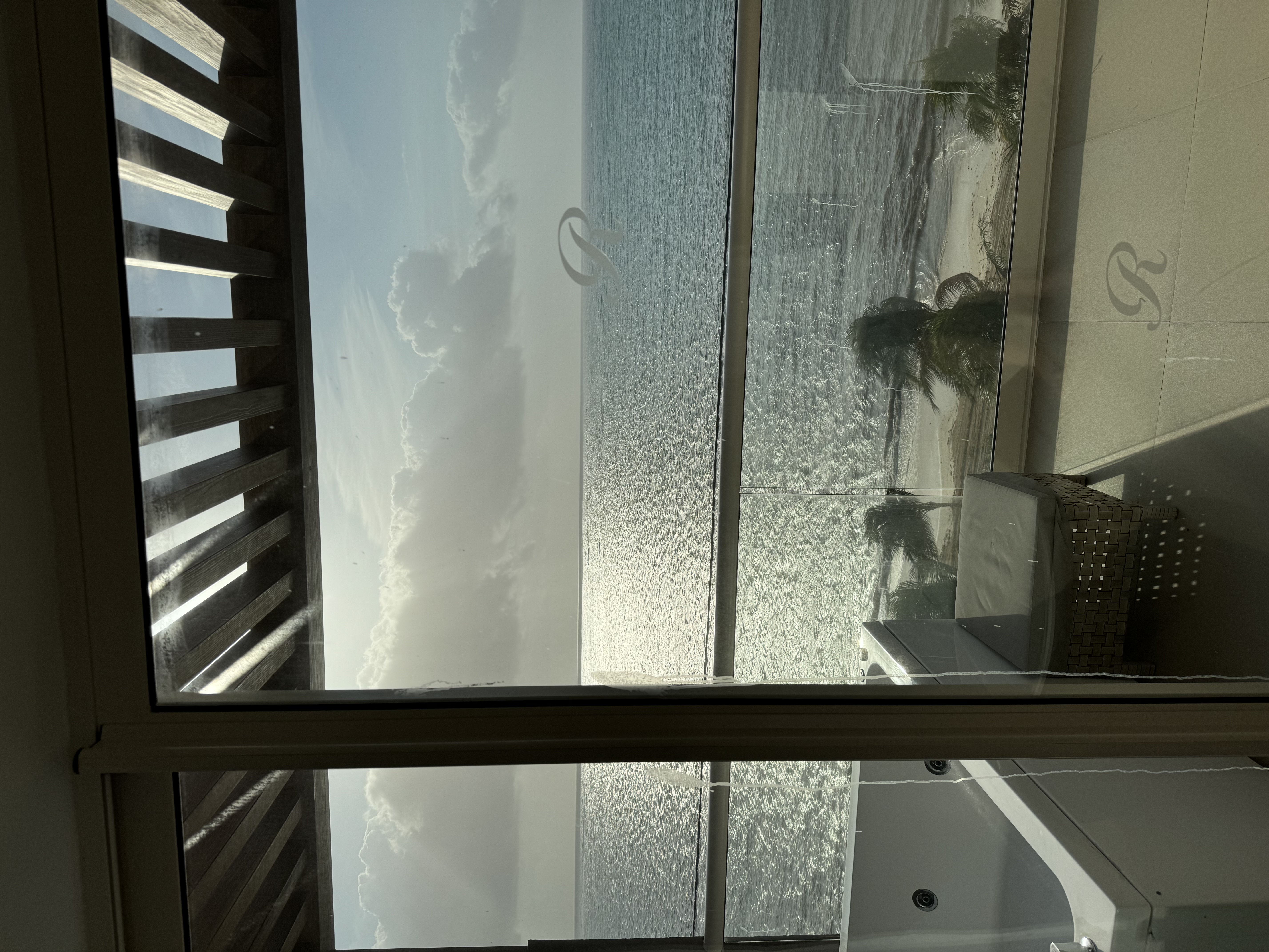 A view looking off of a balcony with a spa at a calm ocean with the sun shining.