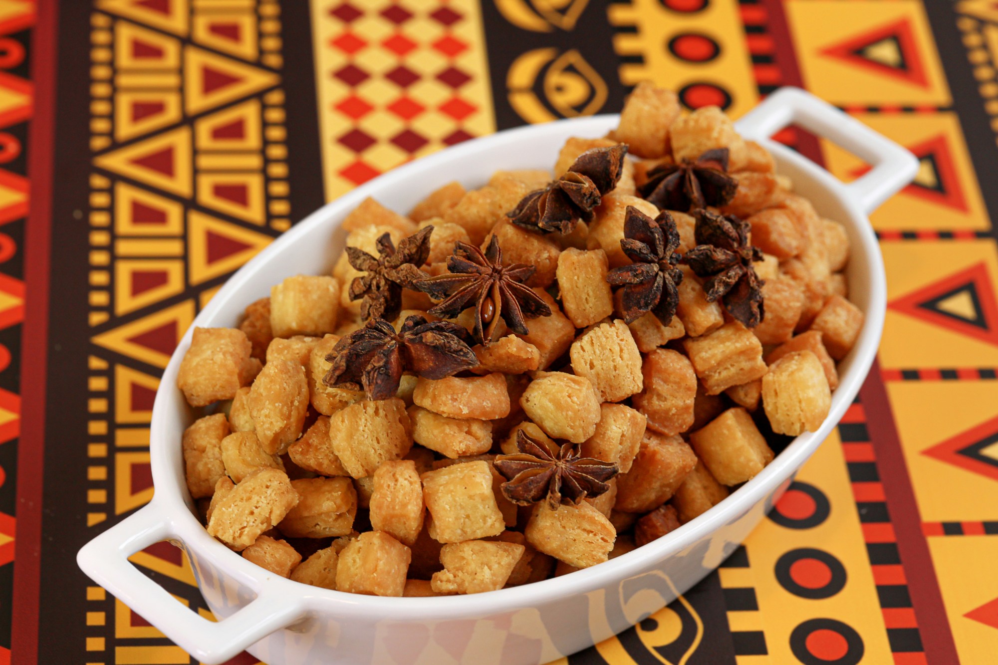 A bowl of small biscuits in a white bowl on a vibrant red, orange, yellow and black patterned table cloth.