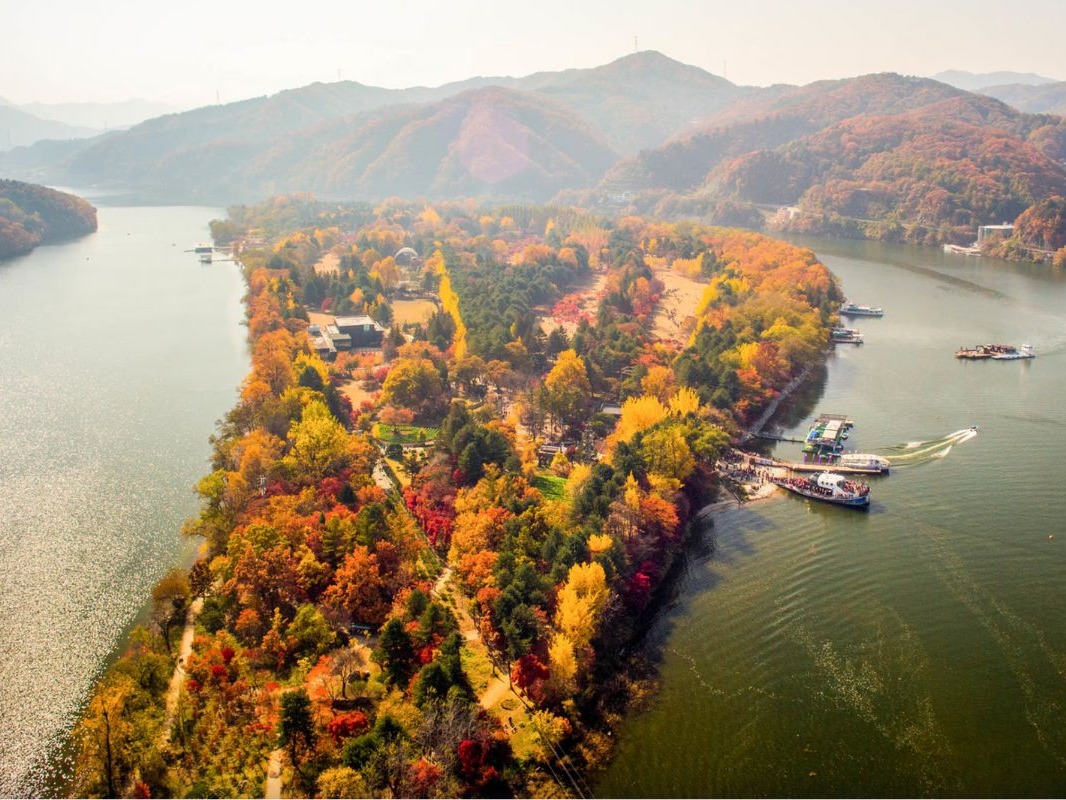 An aerial view of a vibrant autumn landscape with colorful trees, a body of water, and boats near a dock.