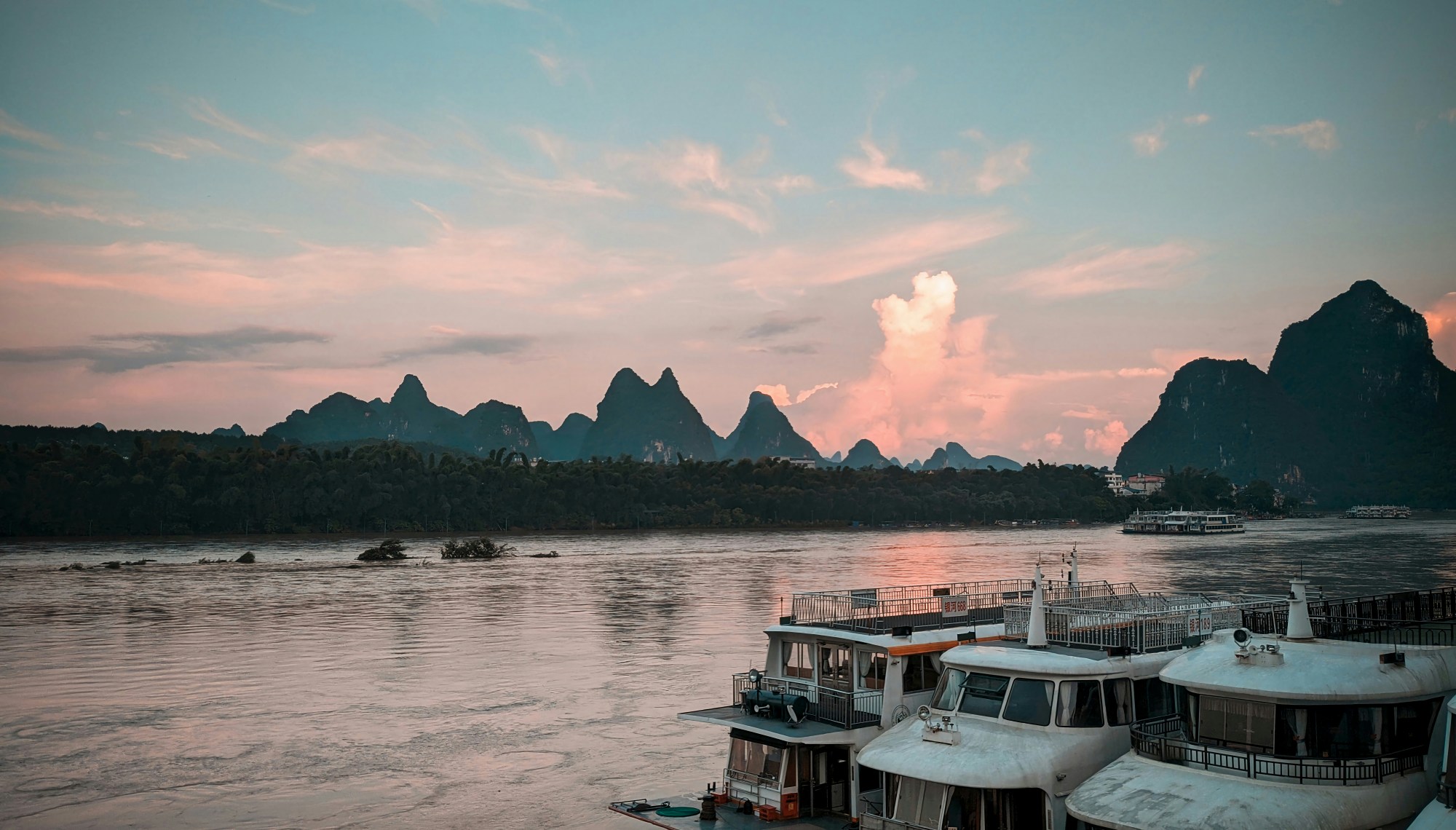 Boats docked in the water at sunset with the silhouette of the mountains across the water against the sky.