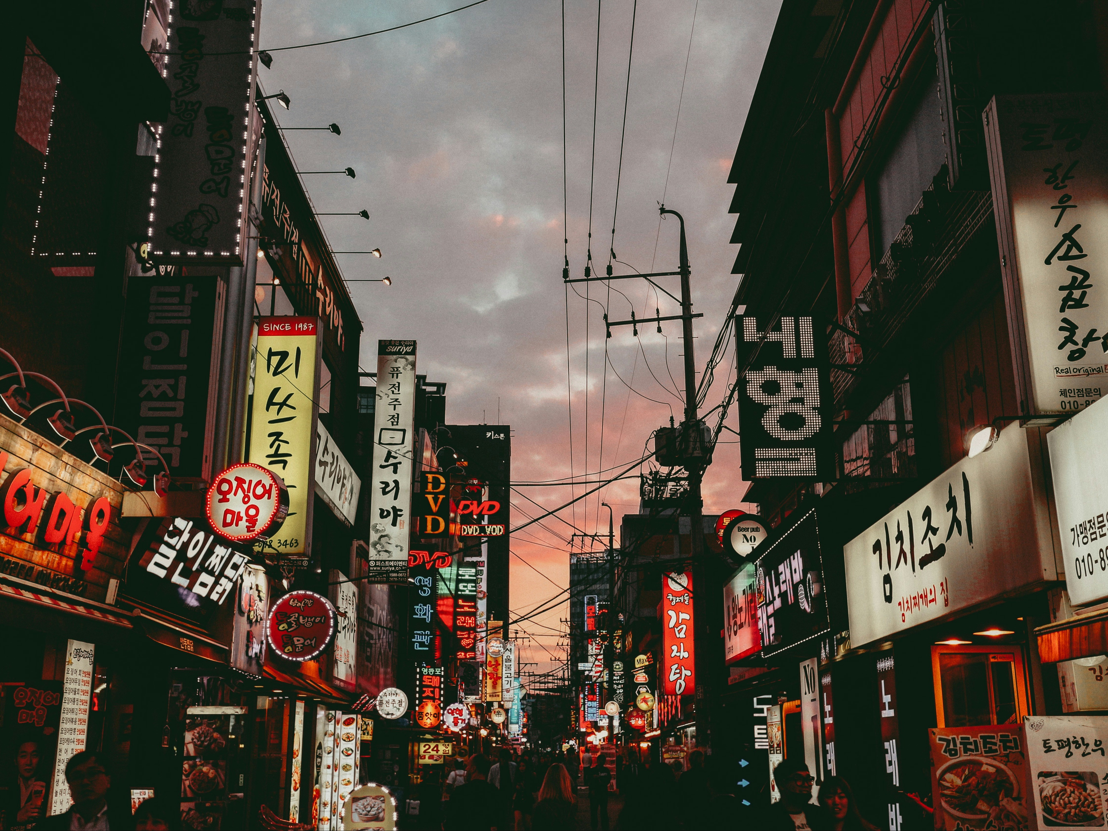 A bustling street at dusk, illuminated by vibrant signs in Korean script.
