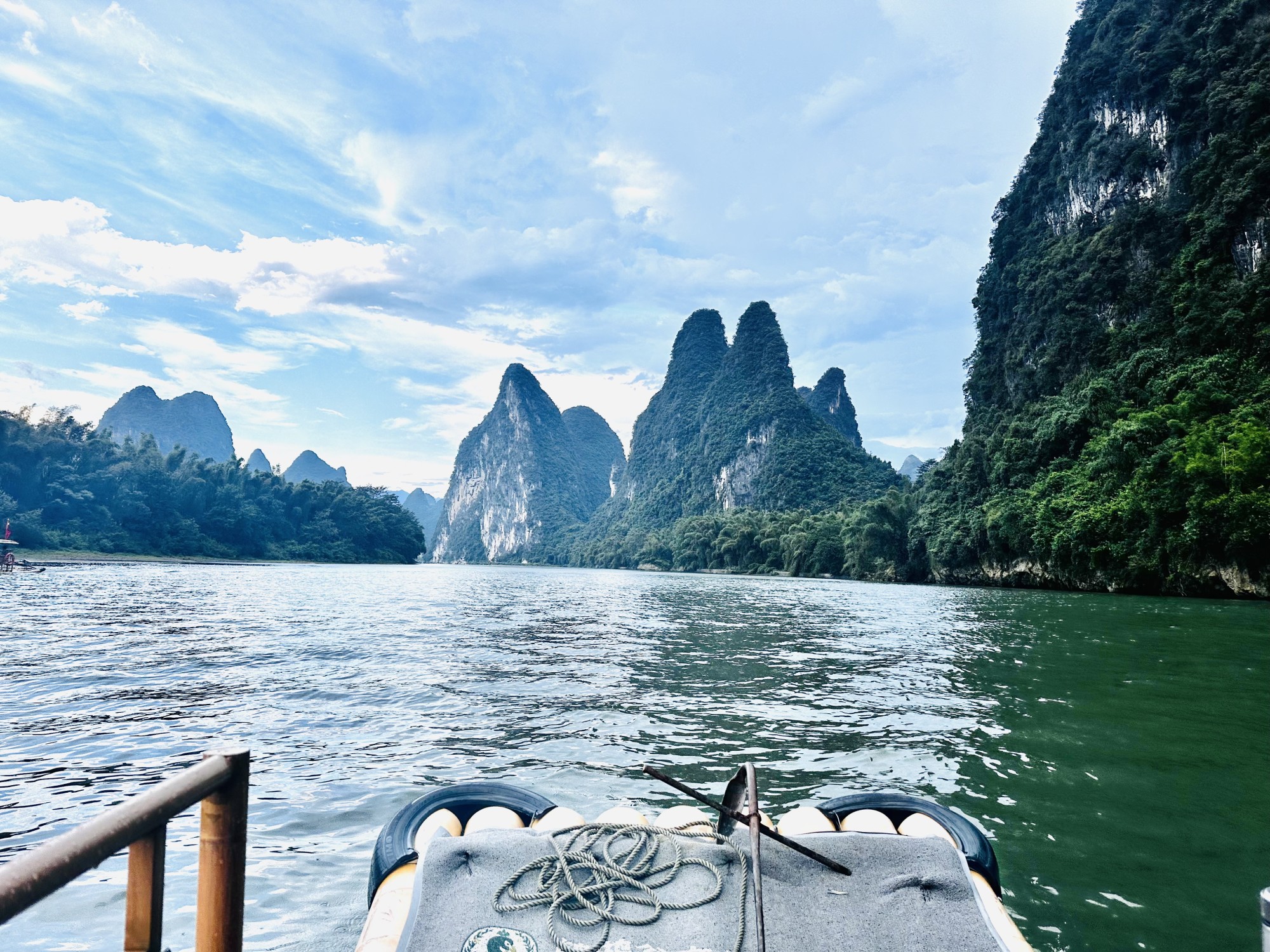 A view overlooking the bow of a boat on the Bamboo River Cruise looking out onto the water with mountains ahead.