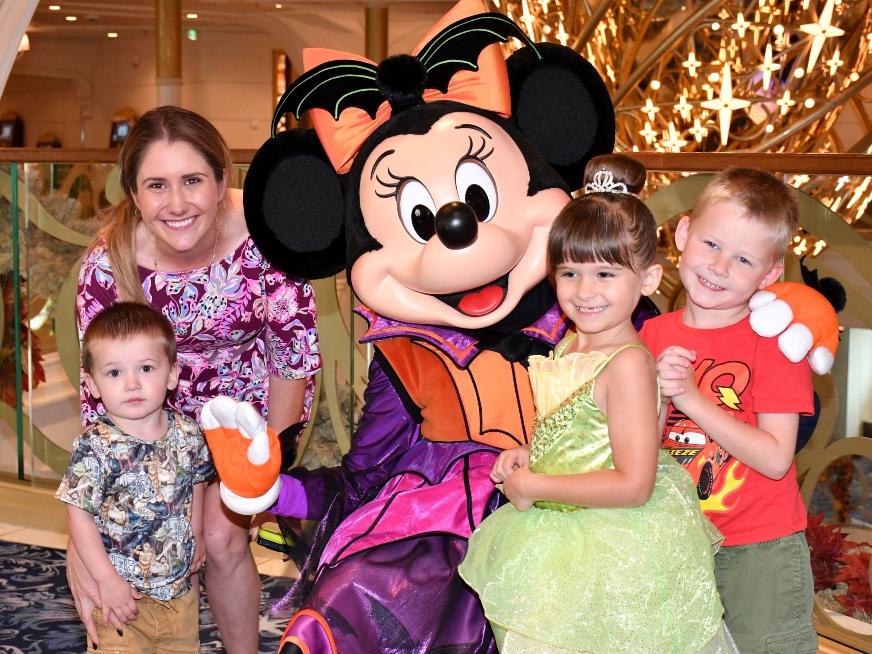 A group of individuals posing with a character dressed as Minnie Mouse indoors with a decorative background.