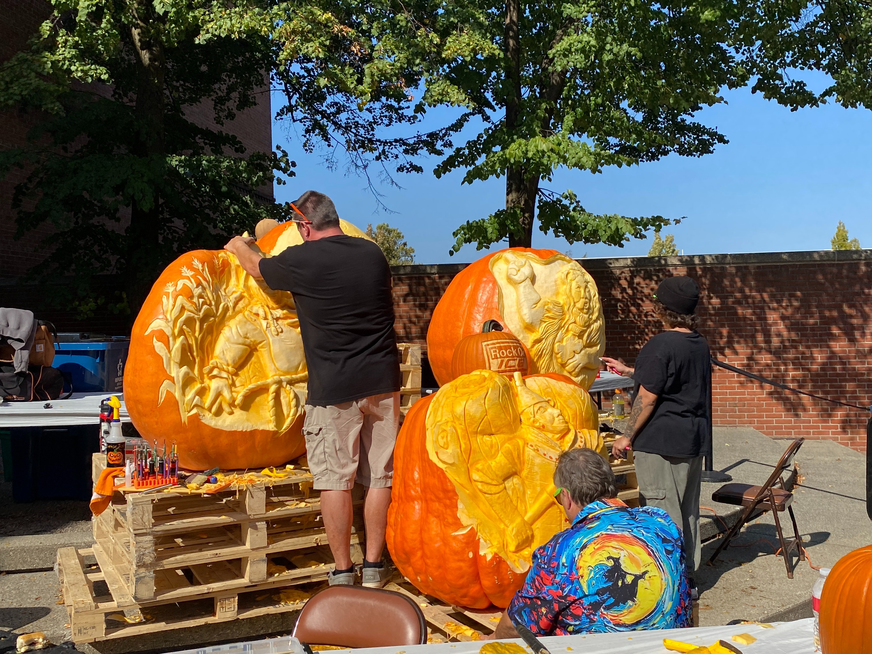 Two individuals are carving large pumpkins at an outdoor event