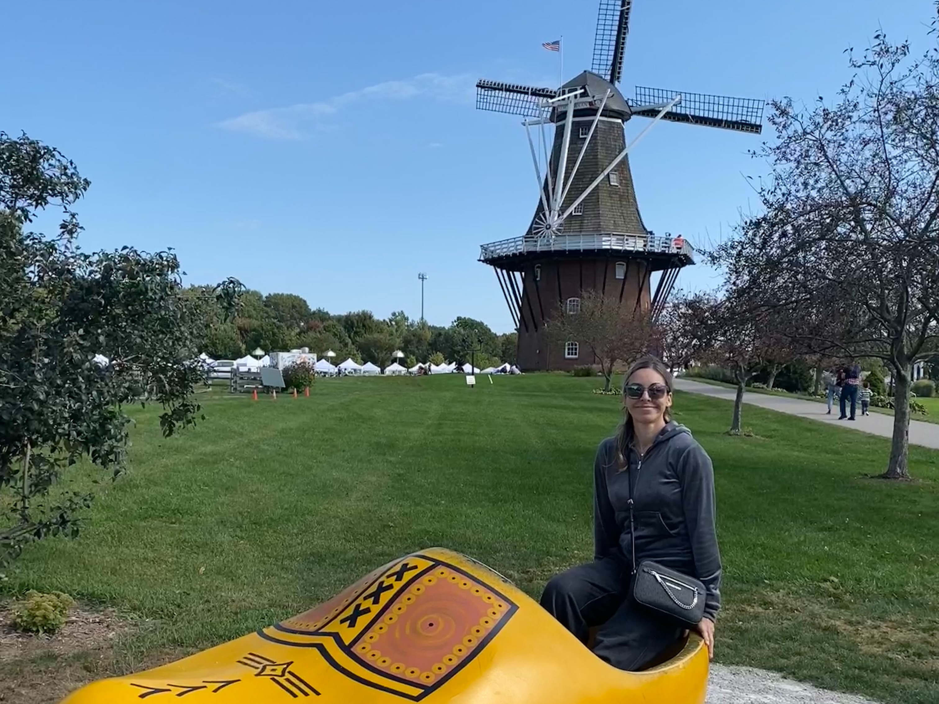 An individual sitting on a large yellow clog in front of a windmill under a clear sky.