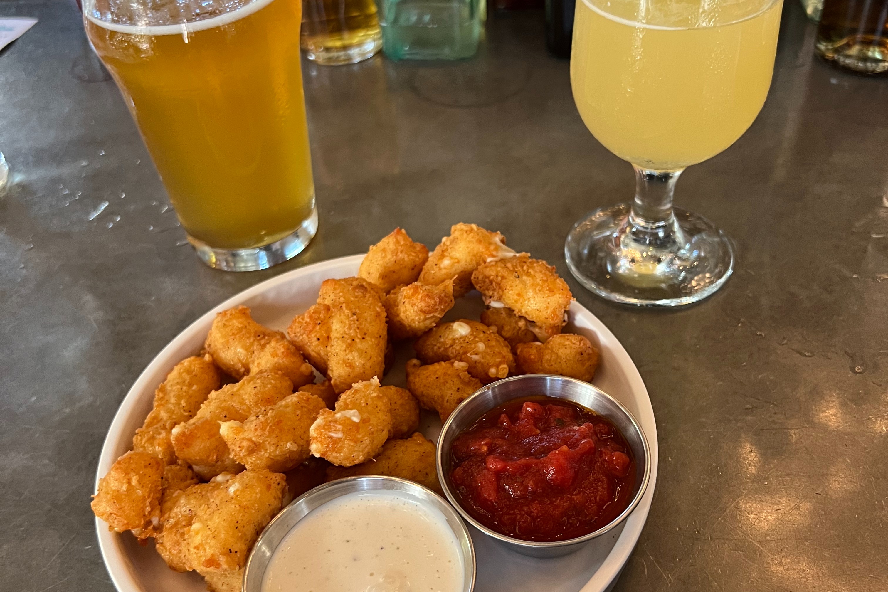 A plate of fried food and dips on a table next to two glasses of beer