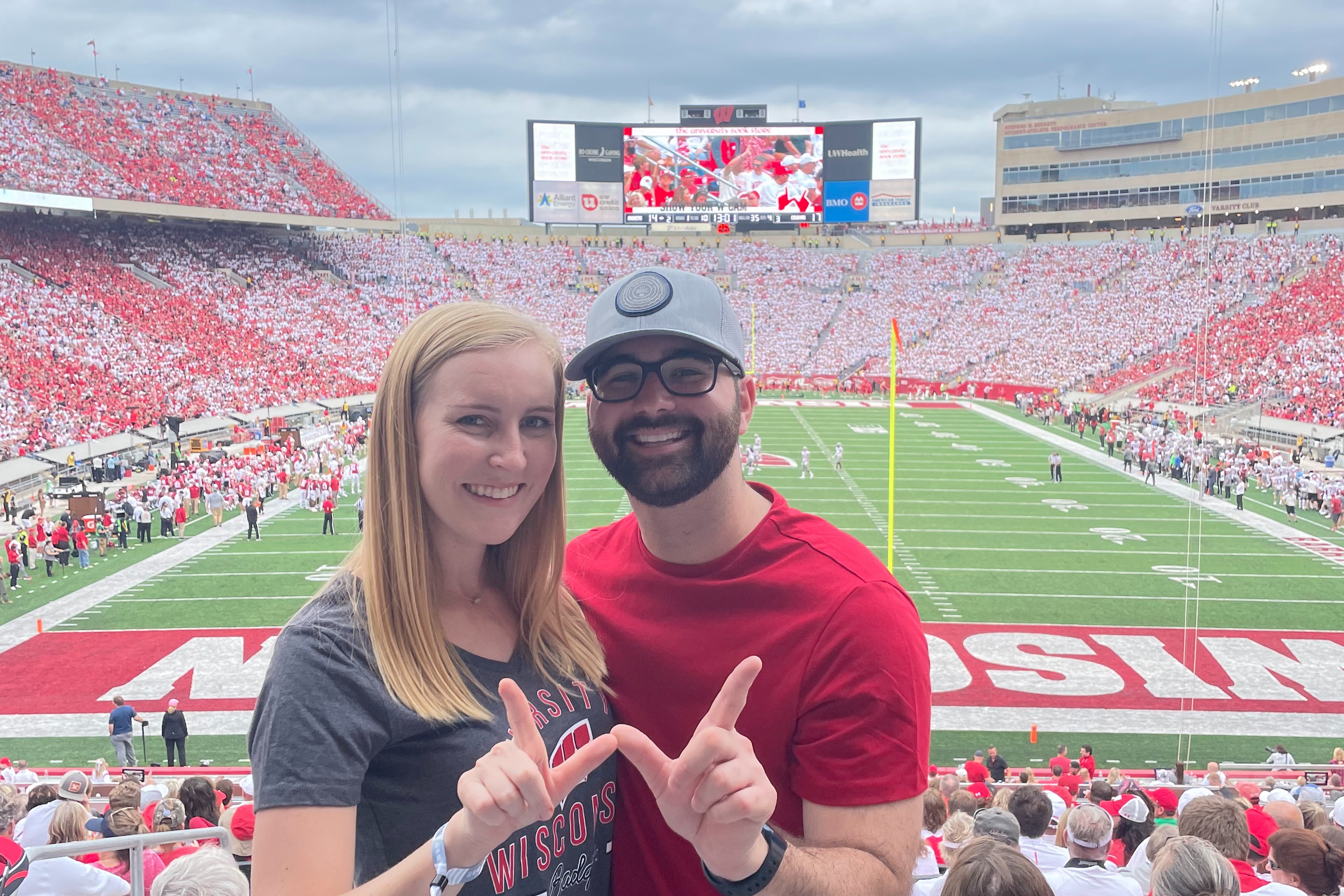Two people posing for a photo together in a football stadium with a view of the field in the background