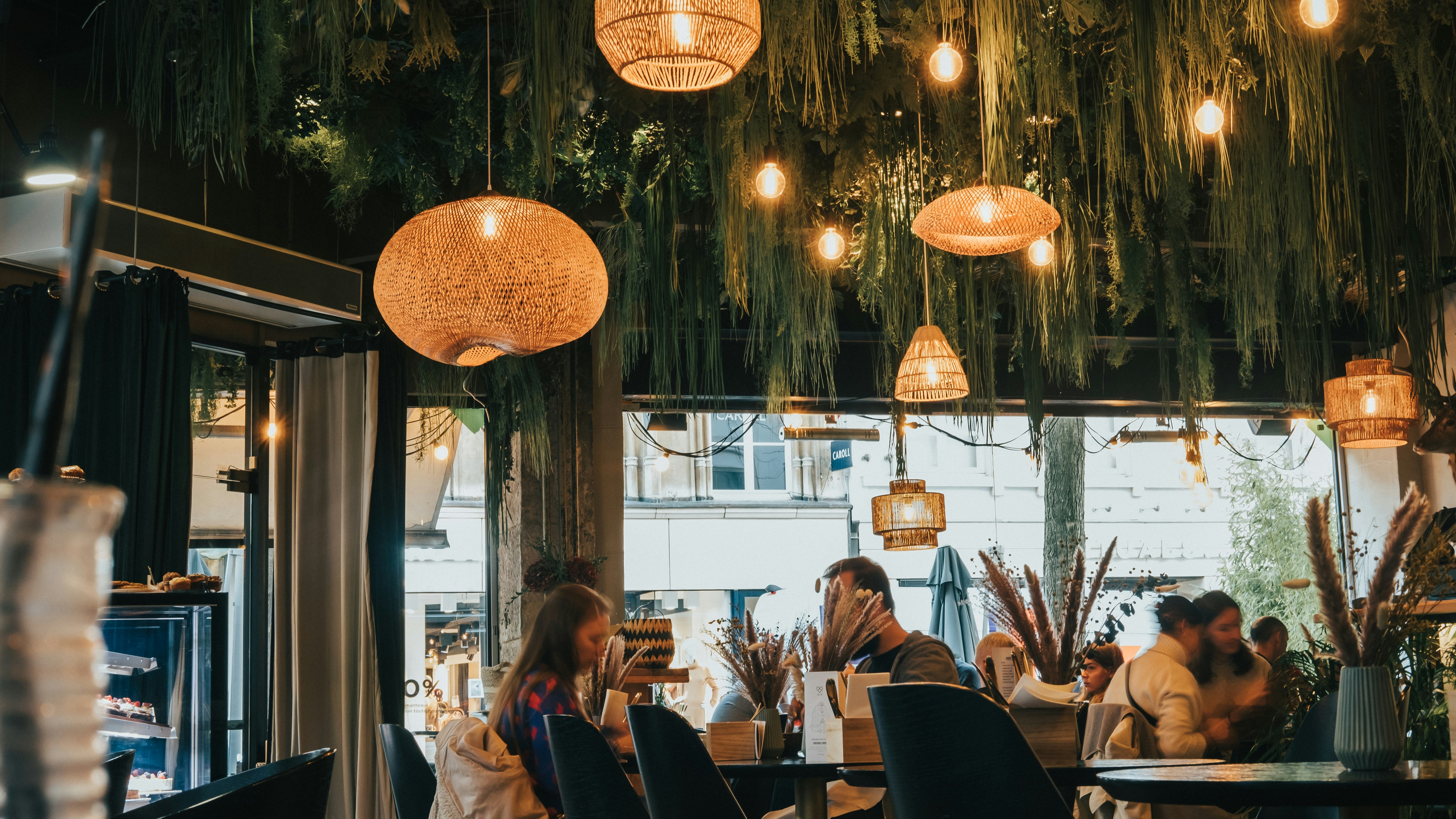 Interior of a restaurant with people sitting at tables and pendant lights hanging overhead.