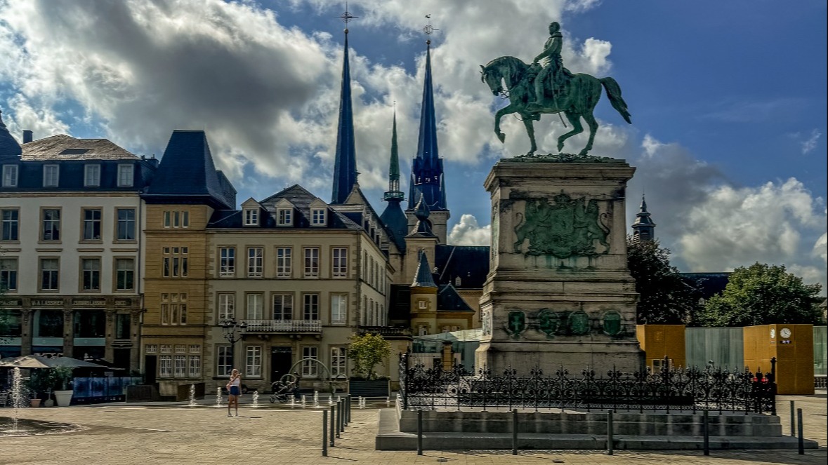 A plaza with historic buildings at the edges and an elevated statute of a man on a horse.