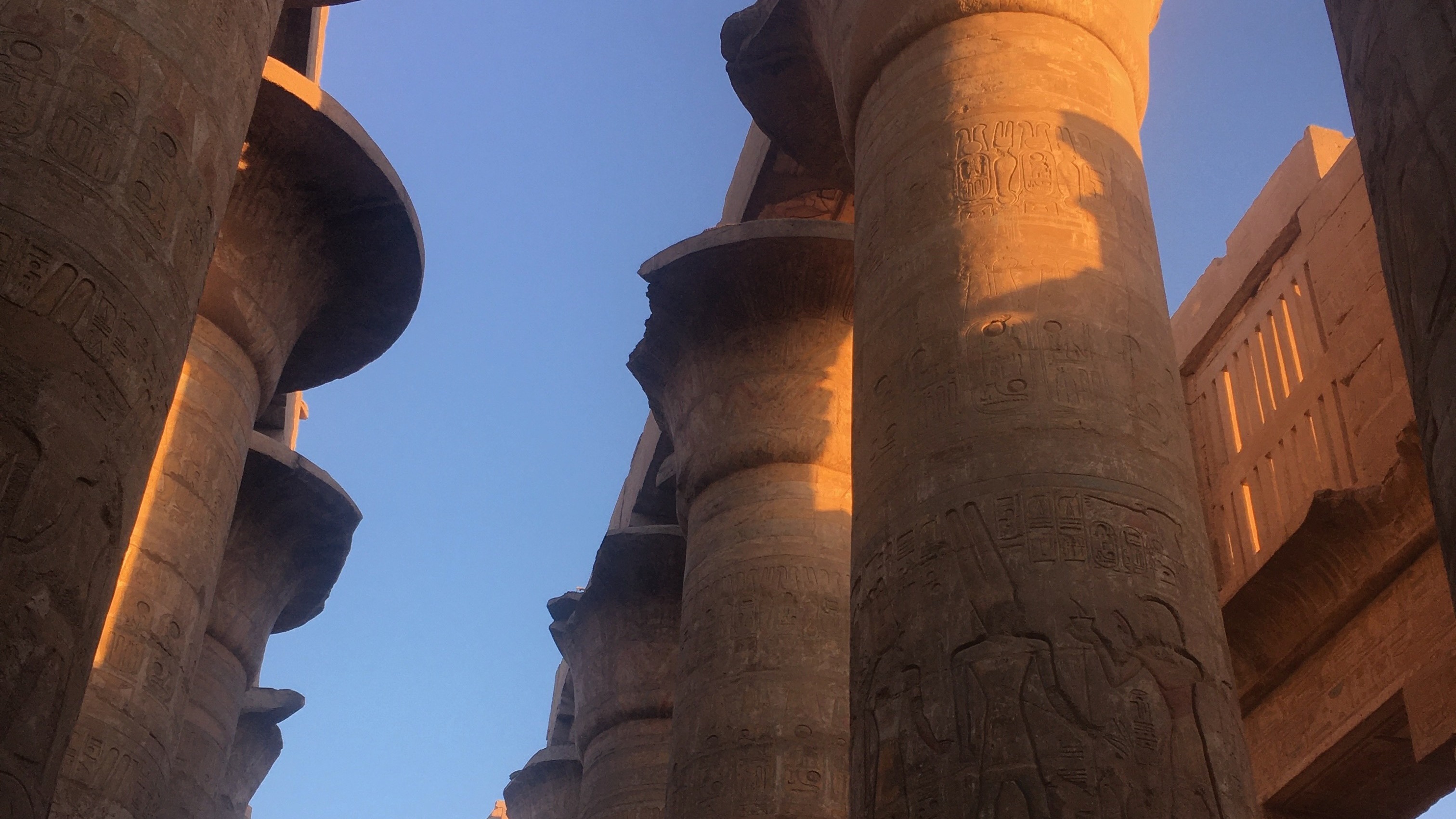 Tall, ancient columns with hieroglyphic carvings set against a clear sky during sunrise or sunset.