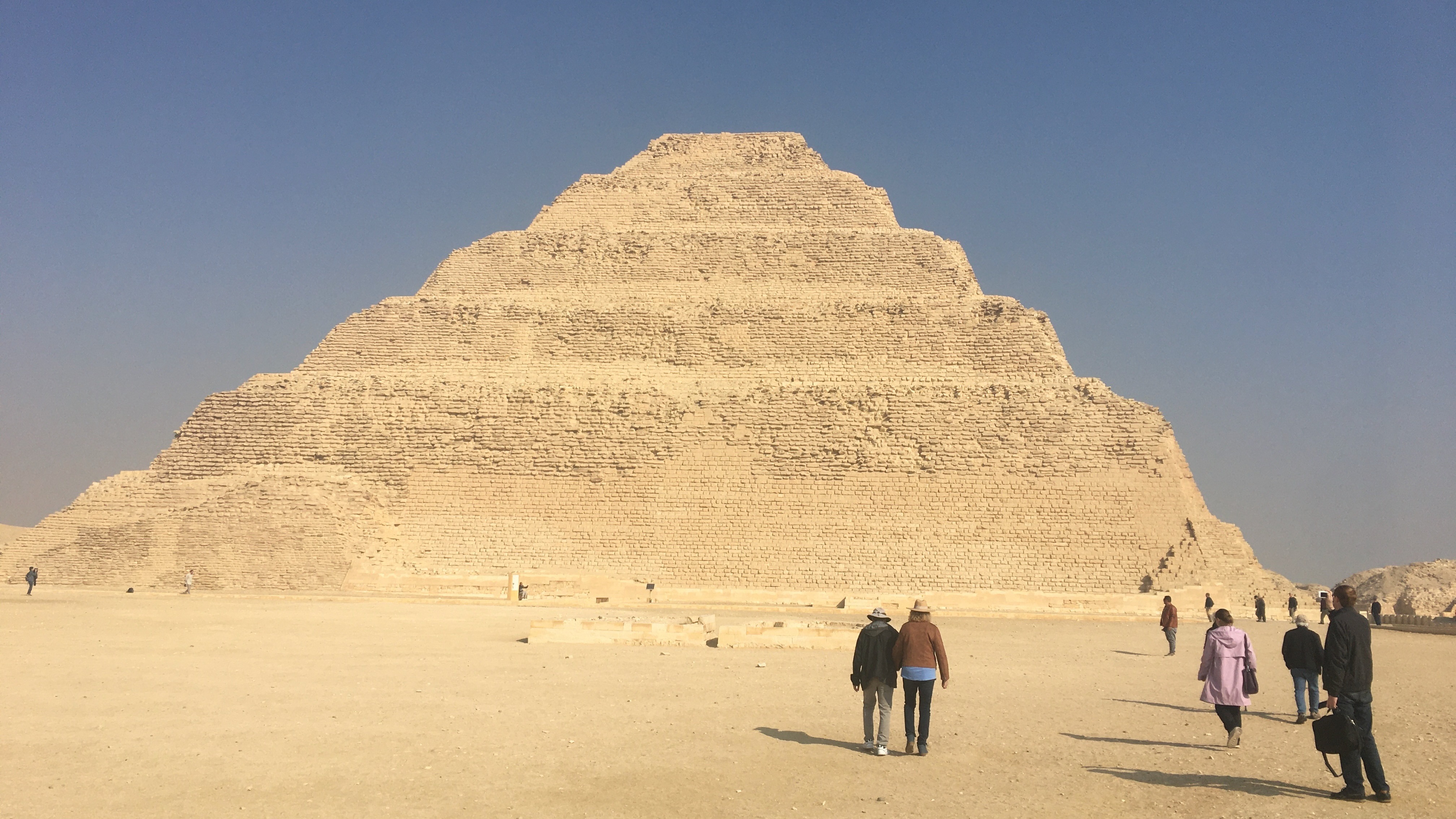A group of individuals walking towards the Step Pyramid of Djoser under a clear sky.