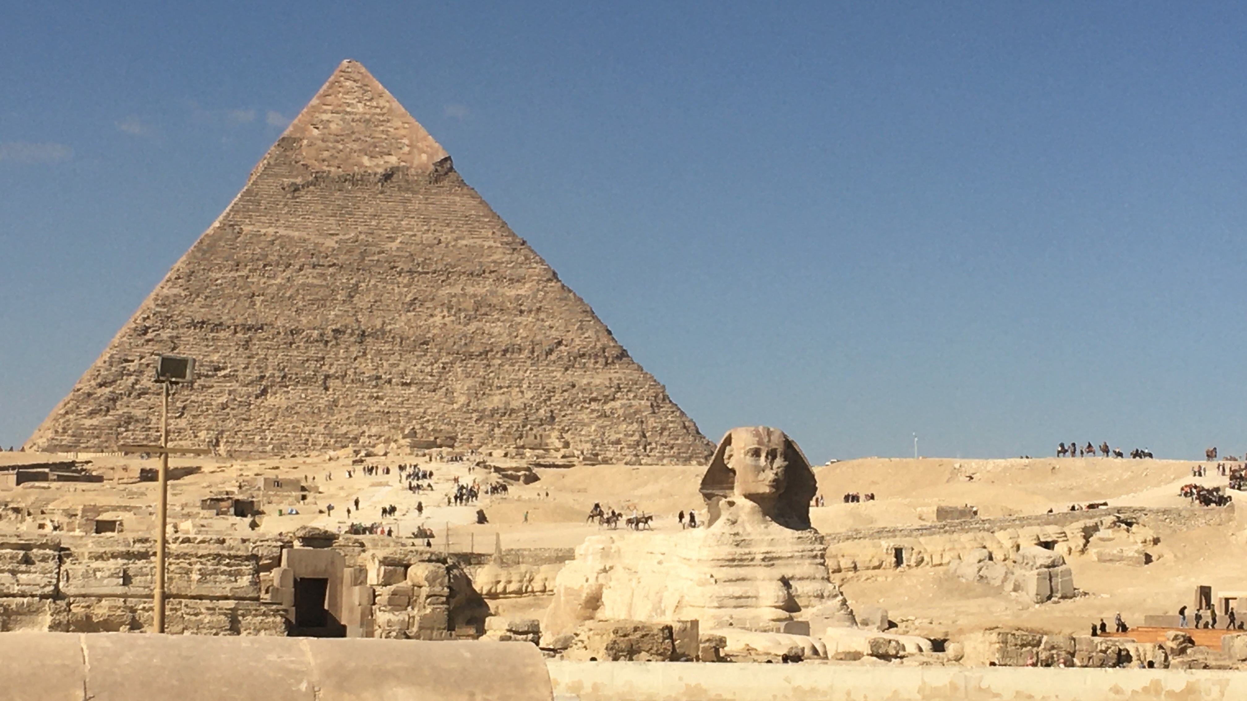 The Great Pyramid of Giza with the Sphinx in the foreground under a clear blue sky.