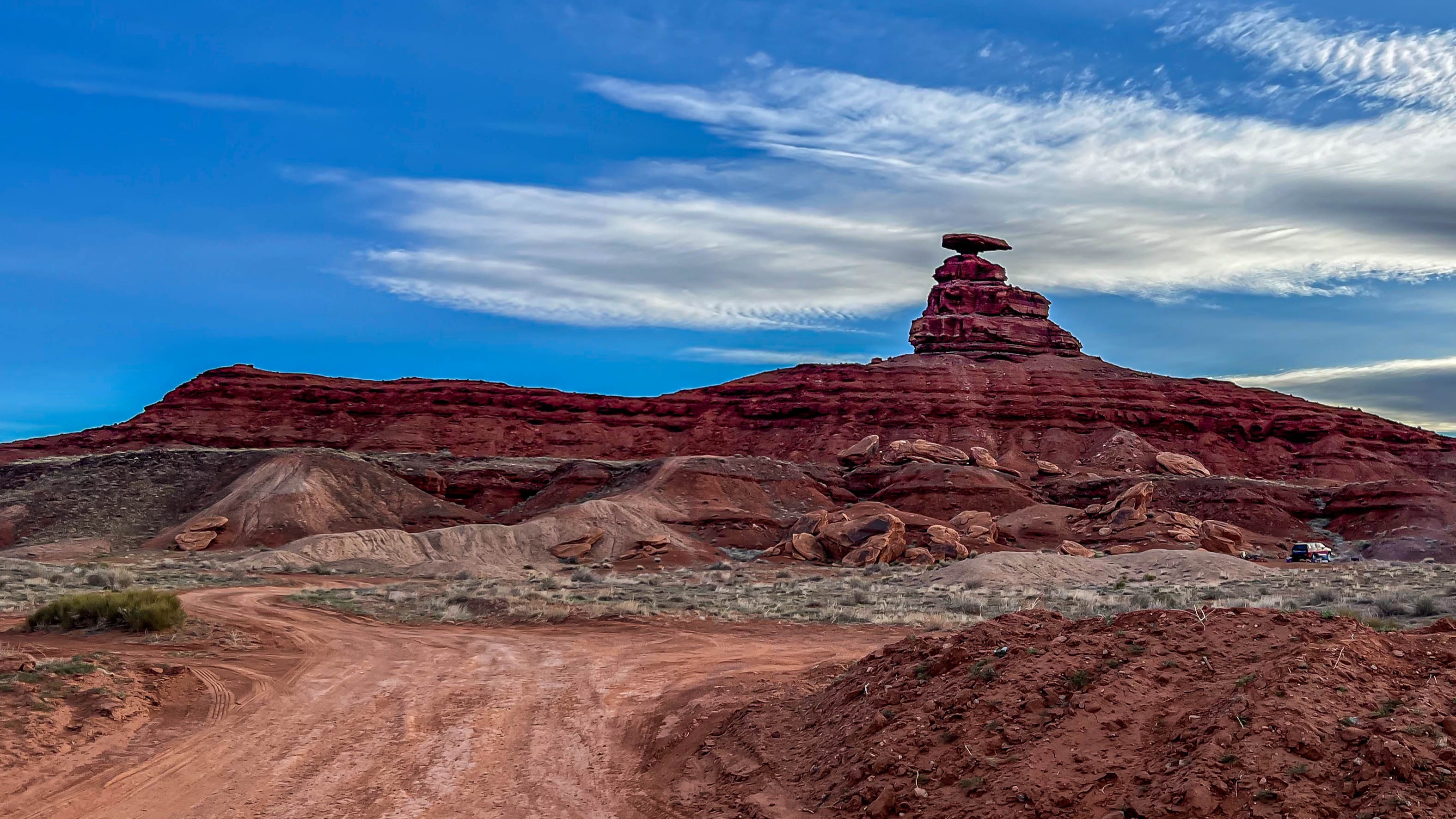 A stack of desert rocks in the distance, silhouetted on a hill, with clear blue skies overhead.