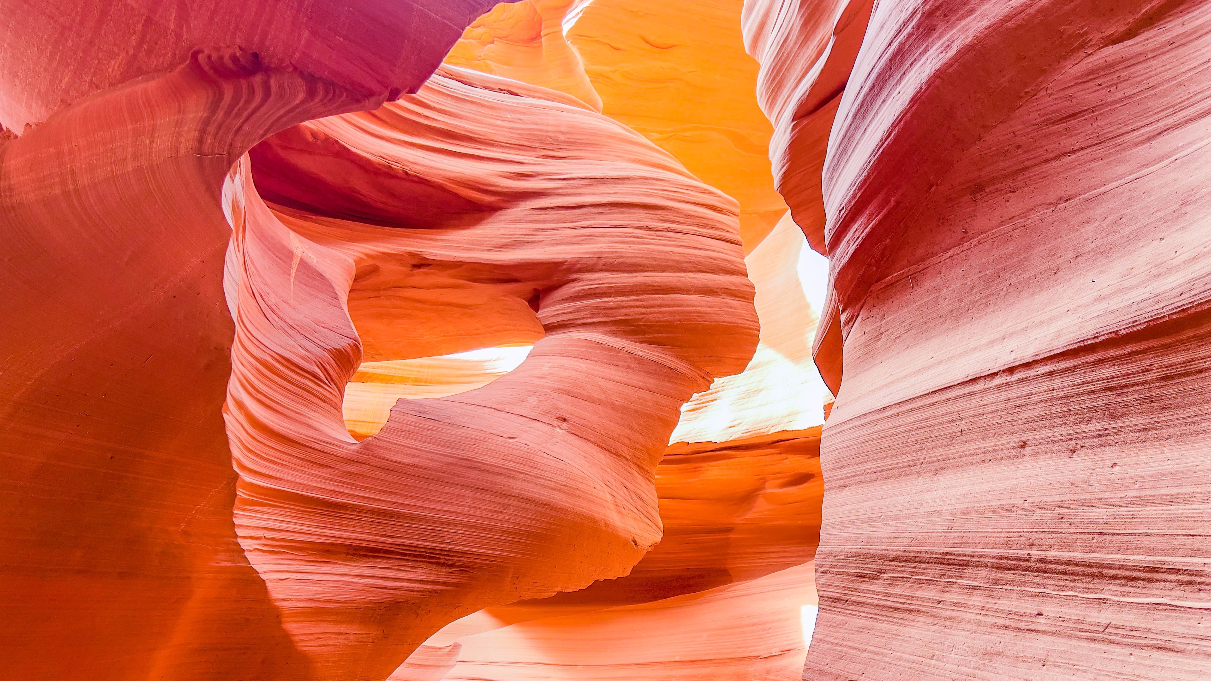 Pink and orange rock formations in a slot canyon with sunlight shining through.