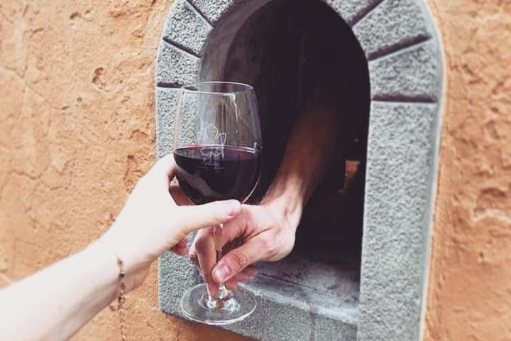 Two people handing a glass of wine between a small window in a wall