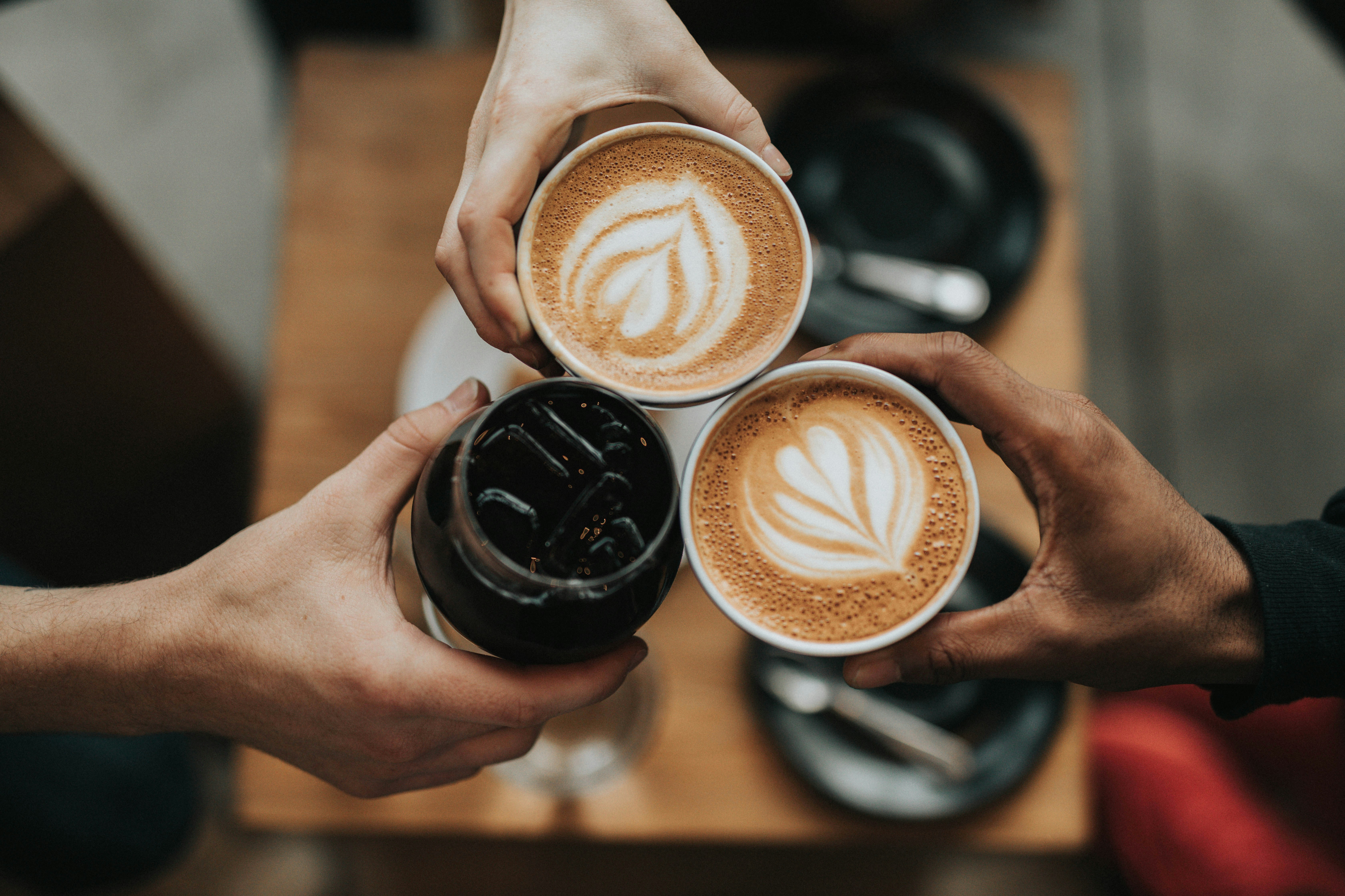 Three hands holding different styles of coffee cups from a top-down view.