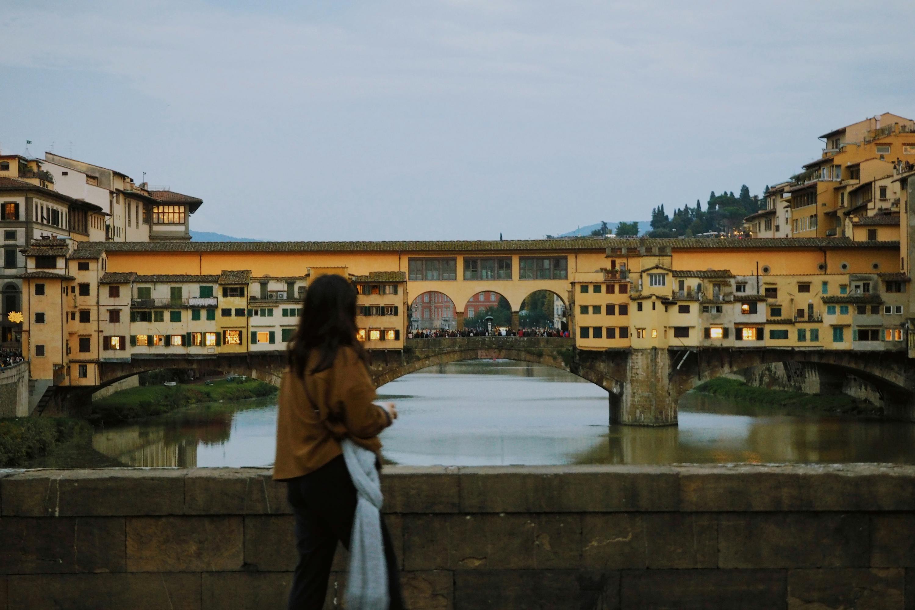 A person standing on a bridge looking out in the distance at a town during the evening