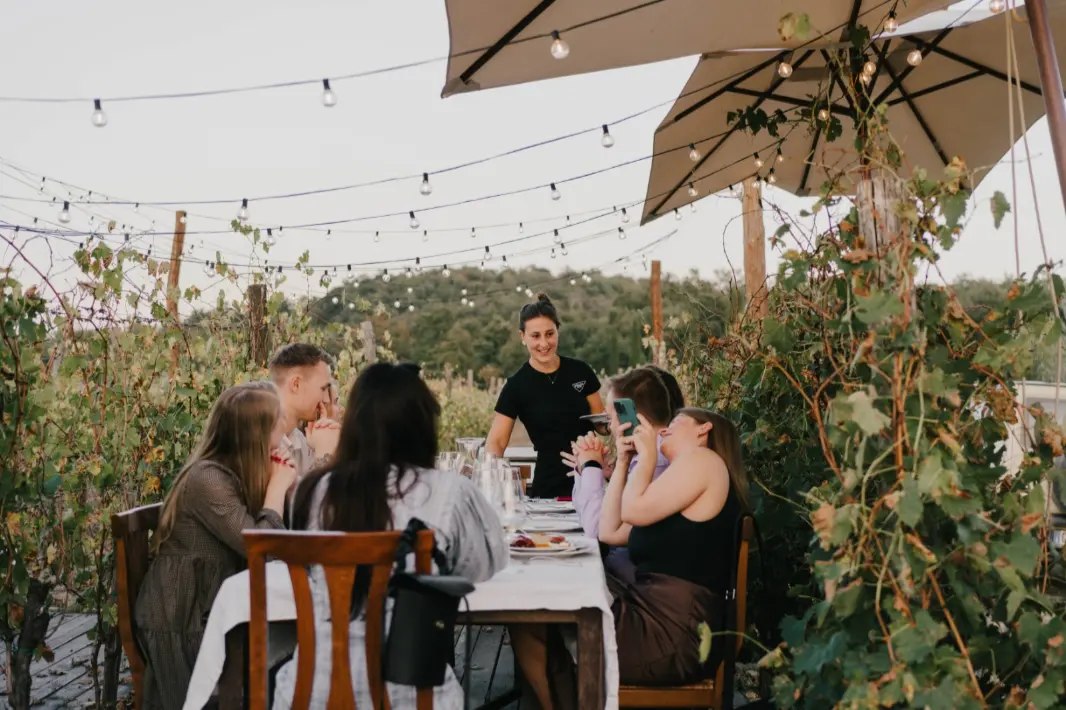 A group of people sitting at an outside dining table with string lights above