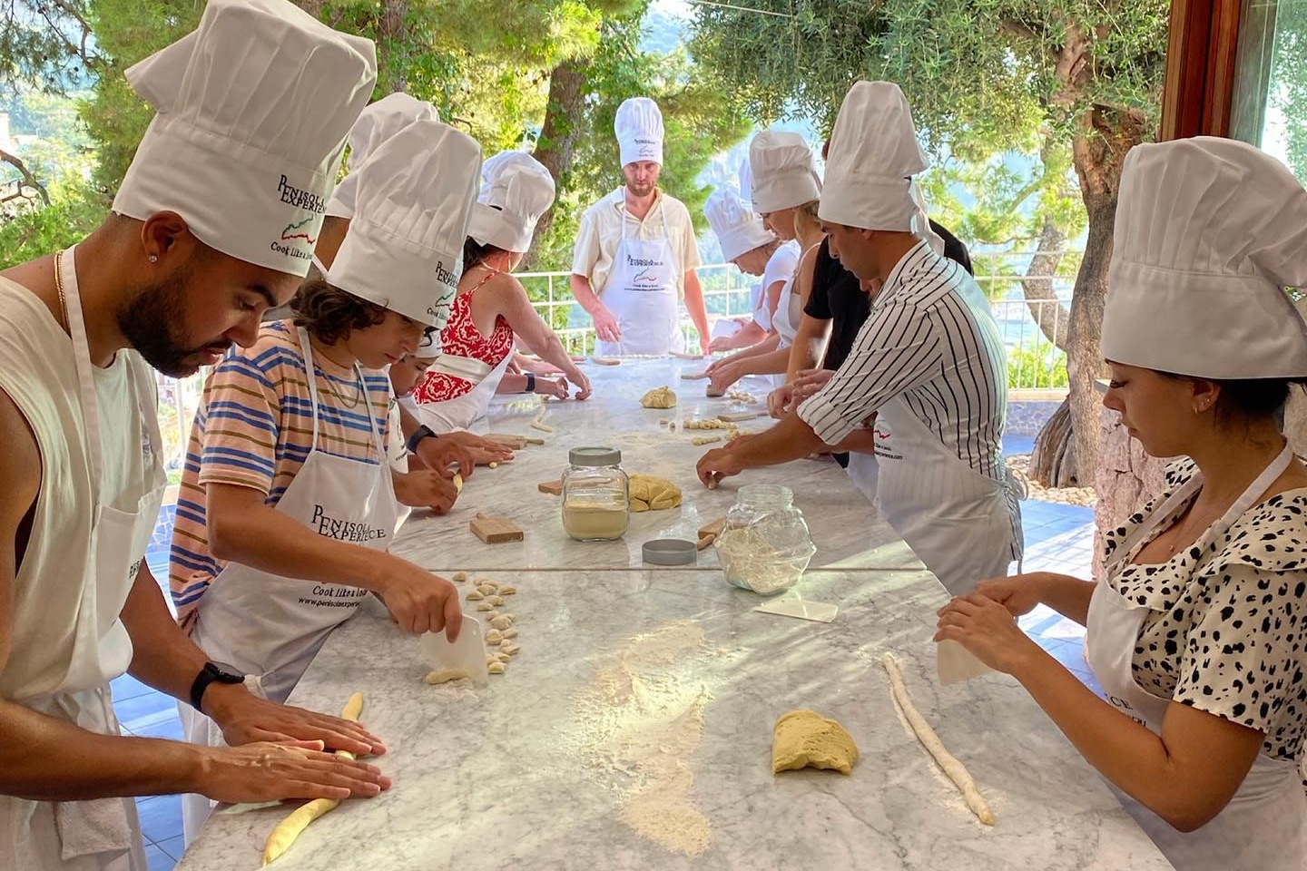 A group of people wearing white chef hats and participating in a pasta making class